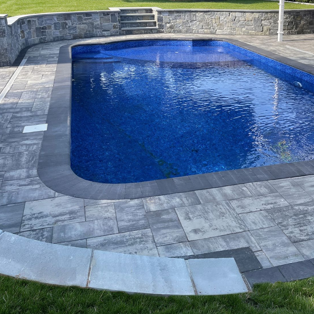 Backyard swimming pool with blue water, stone coping, and a surrounding gray patio.