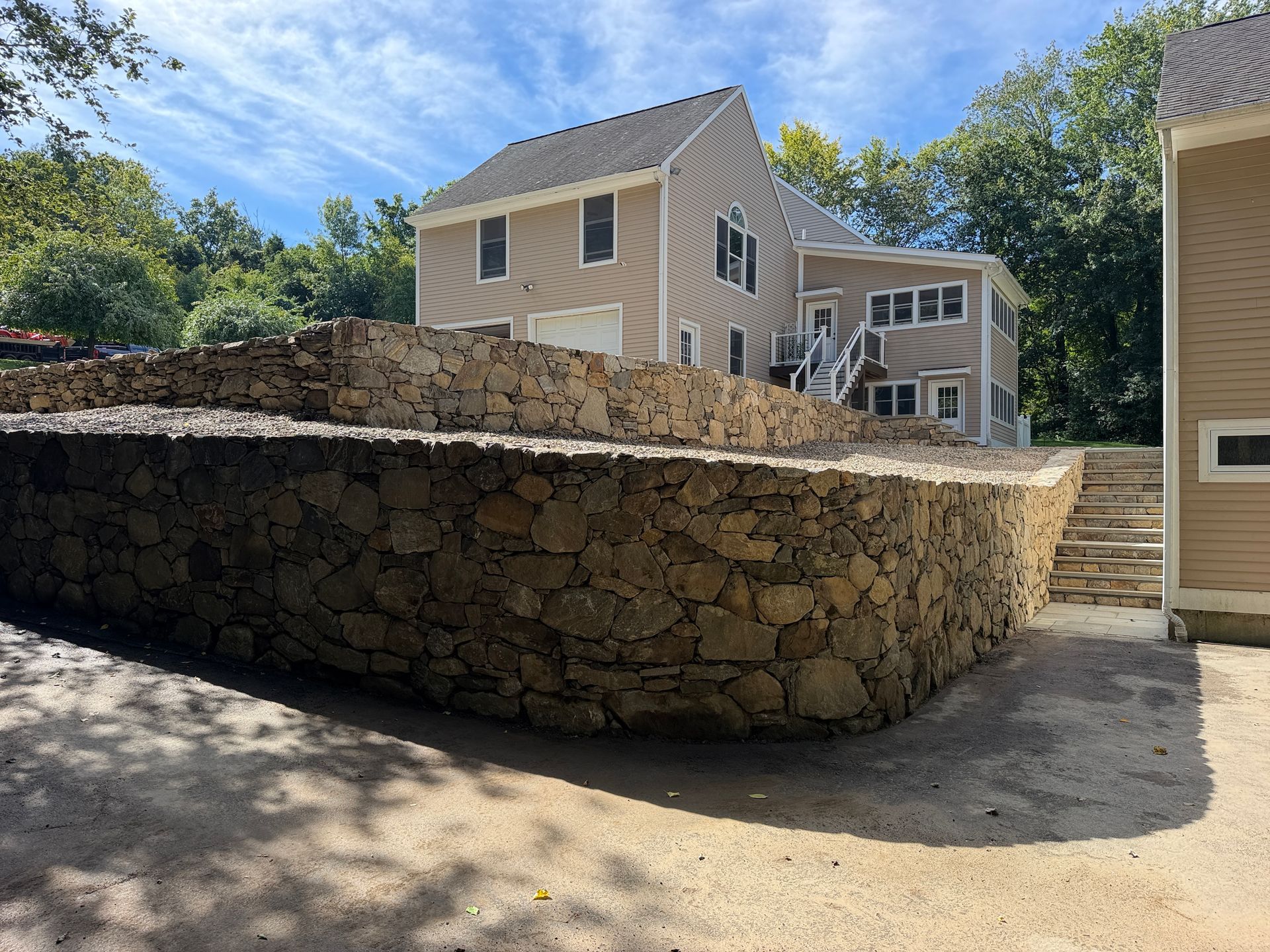 Stone retaining wall in front of tan houses on a sunny residential street.