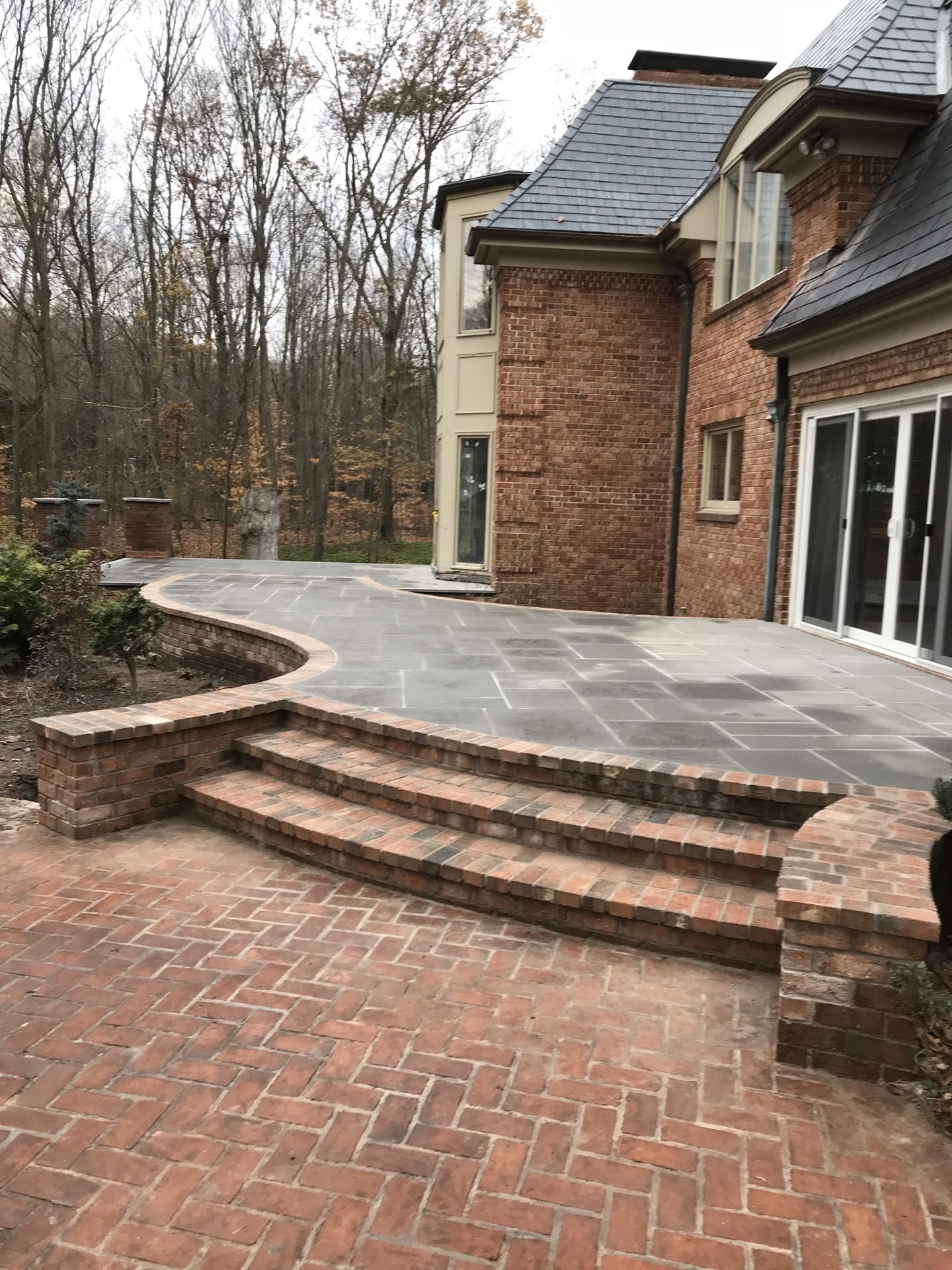 Brick house patio with curved stone steps and wooded background