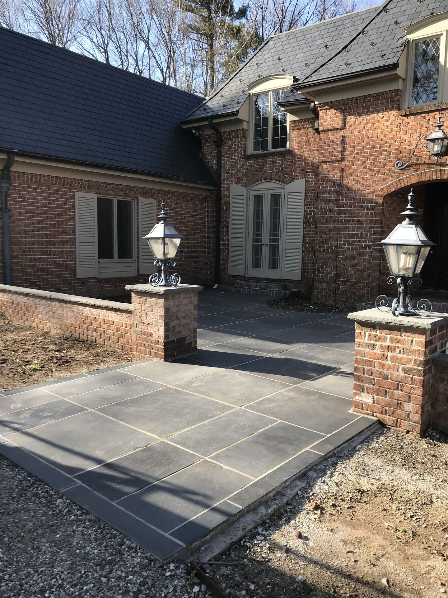 Brick house entry with a paved patio, brick pillars, and lantern-style lights