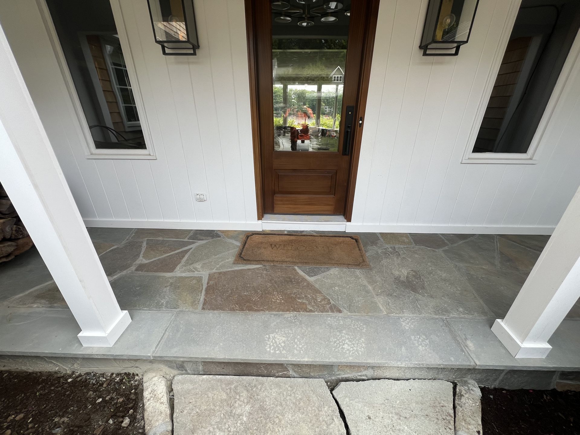 Front porch with stone tile floor, white columns, and a wooden front door with sidelights.