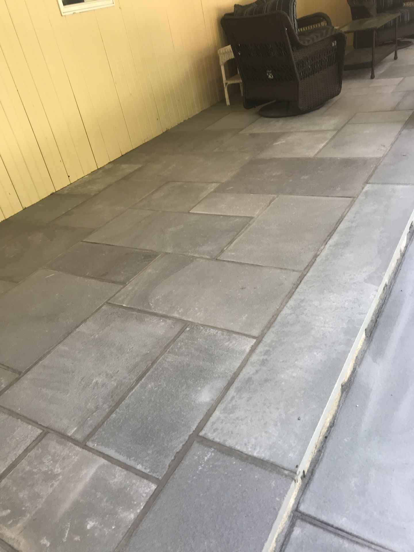 Outdoor patio with gray pavers beside a yellow wall and black grill equipment