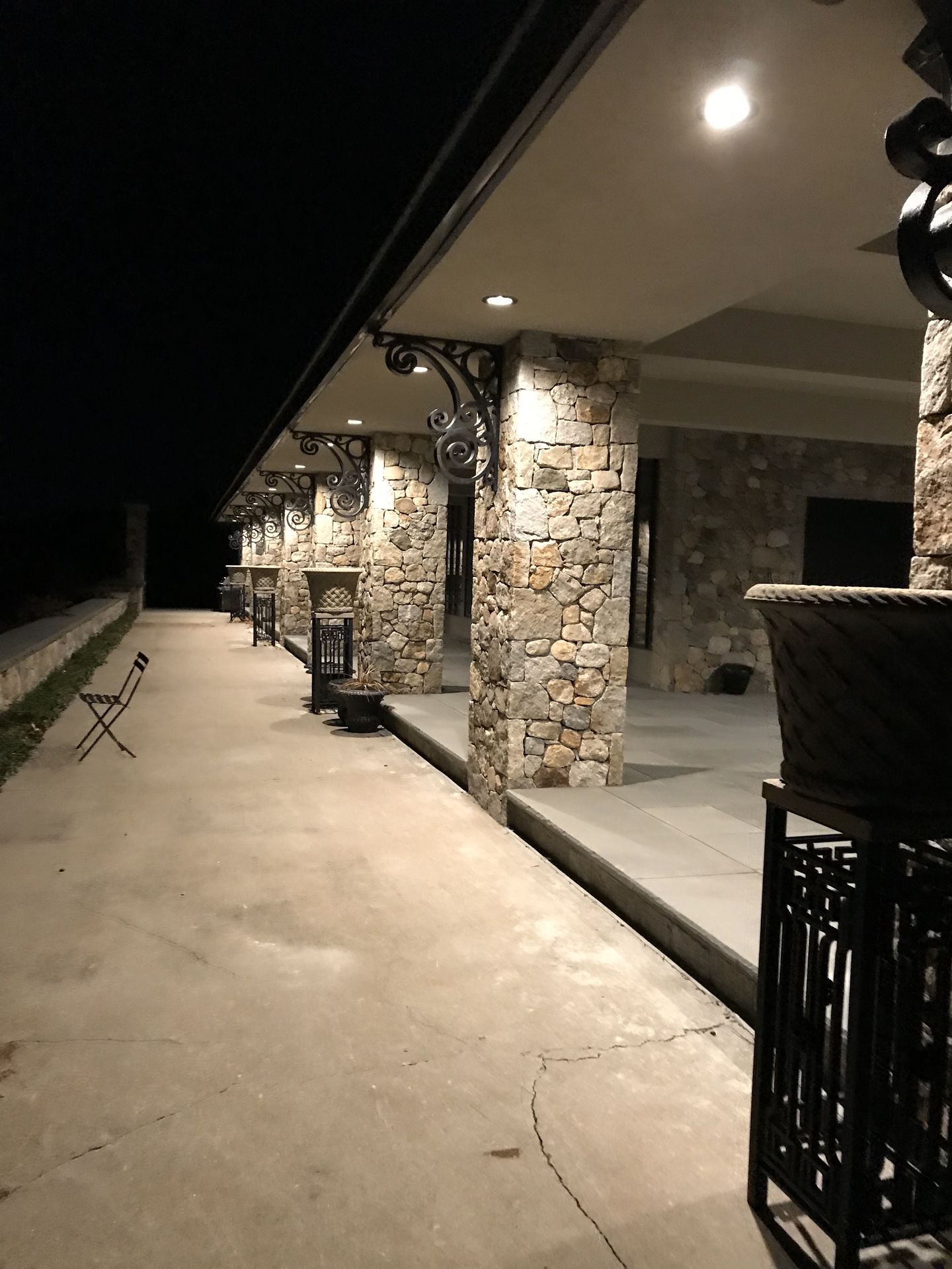 Nighttime covered patio with stone pillars, ceiling lights, and a long concrete walkway.