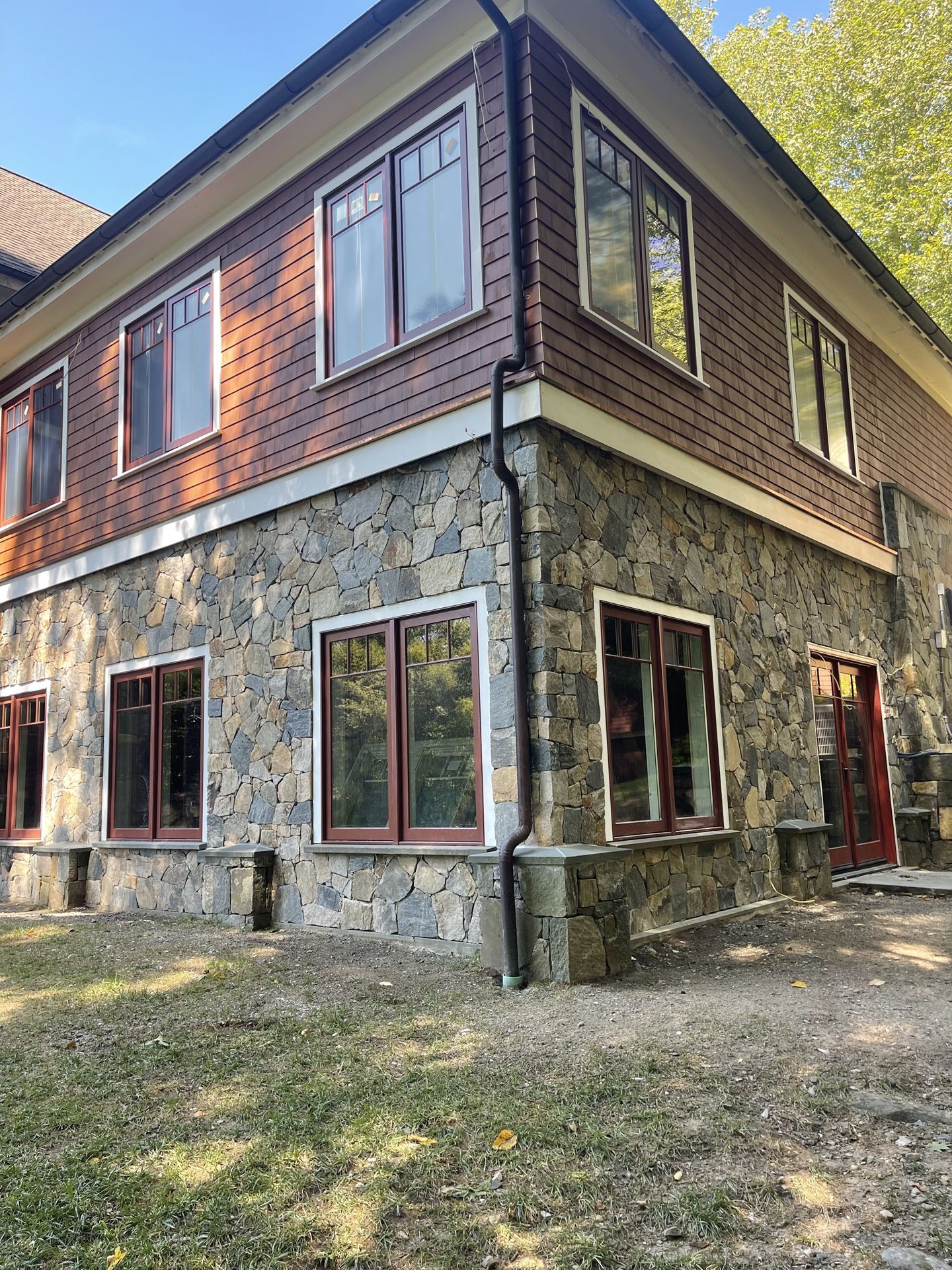 Two-story house with stone lower level, wood upper siding, and many windows in a leafy yard