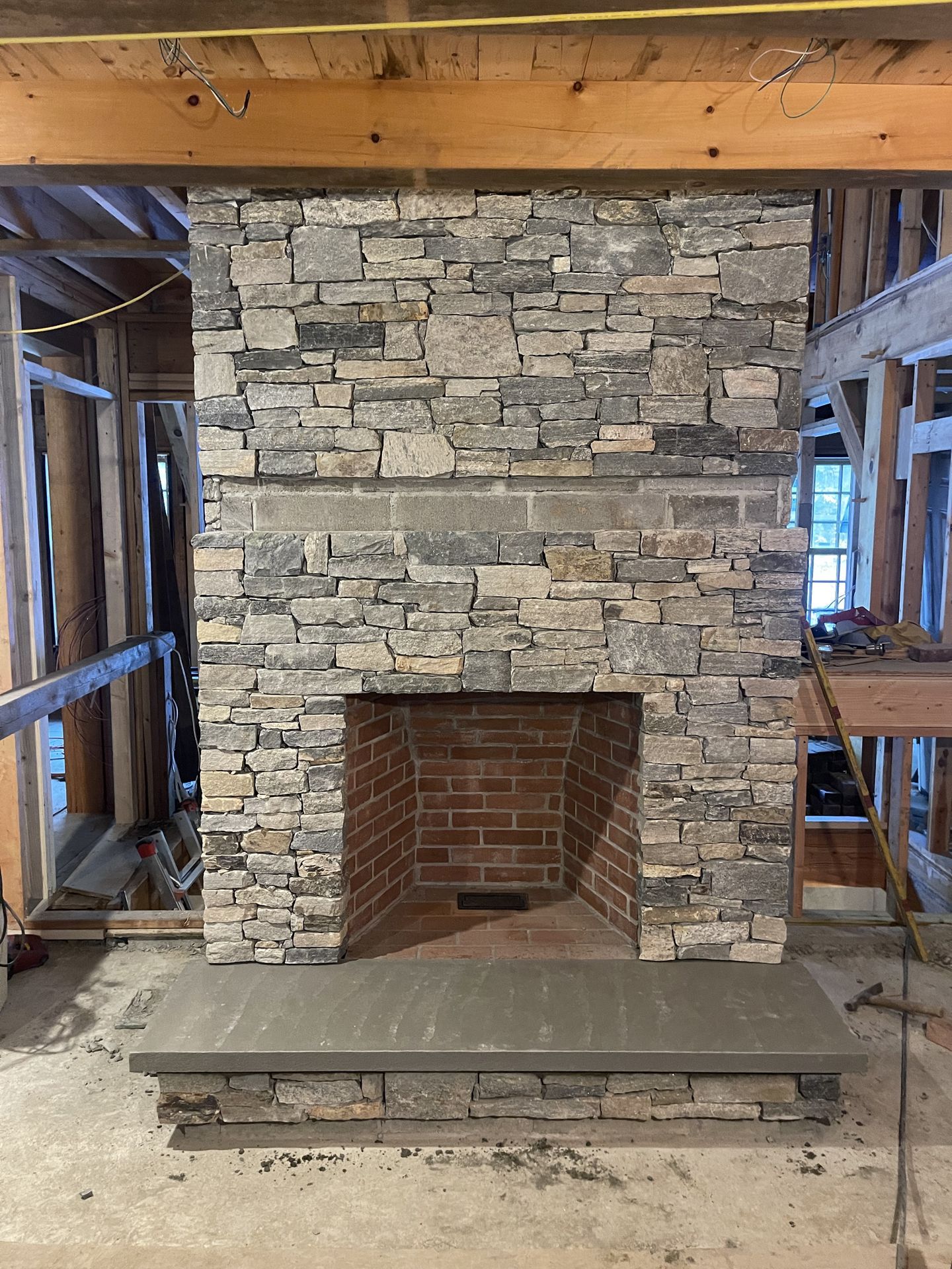 Stone fireplace under construction with brick firebox, surrounded by wooden framing and scaffolding