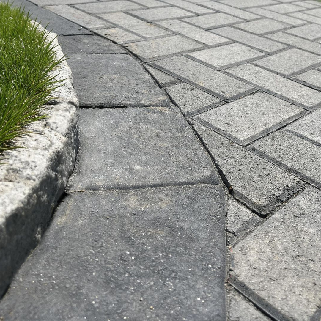 Curved stone walkway beside grass, meeting a gray paved path.