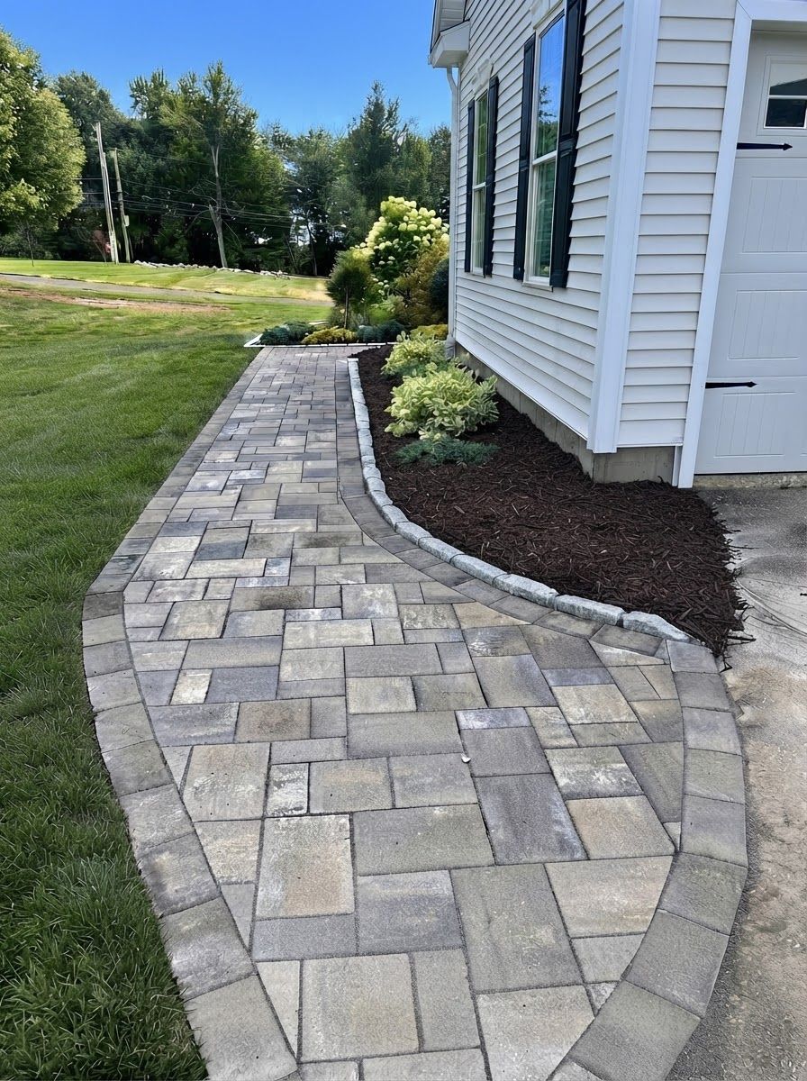 Curved stone walkway beside a white house and landscaped garden under a clear sky