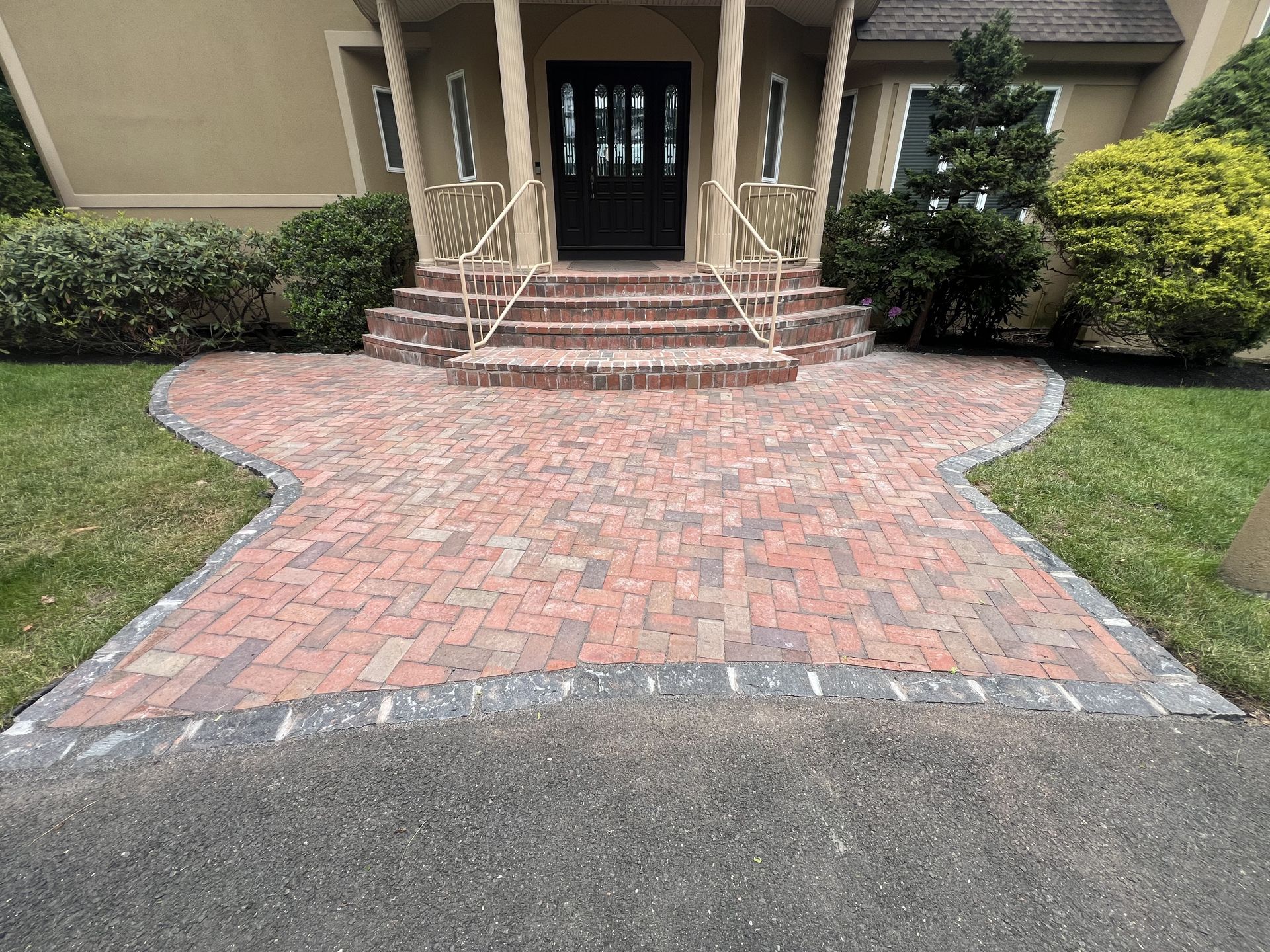 Brick walkway leading to a building entrance with steps, railings, and shrubs on both sides.