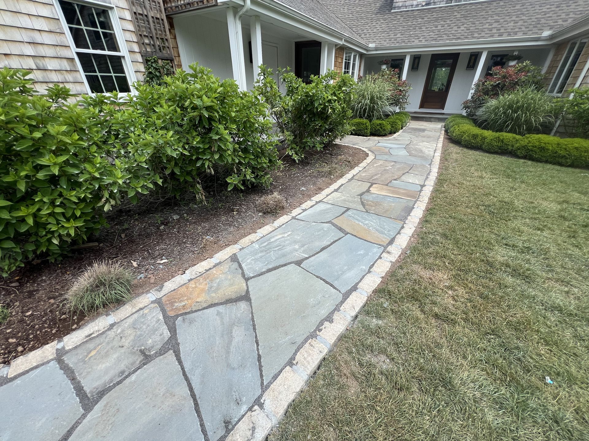 Stone walkway curving through landscaped front yard beside a brick house and shrubs