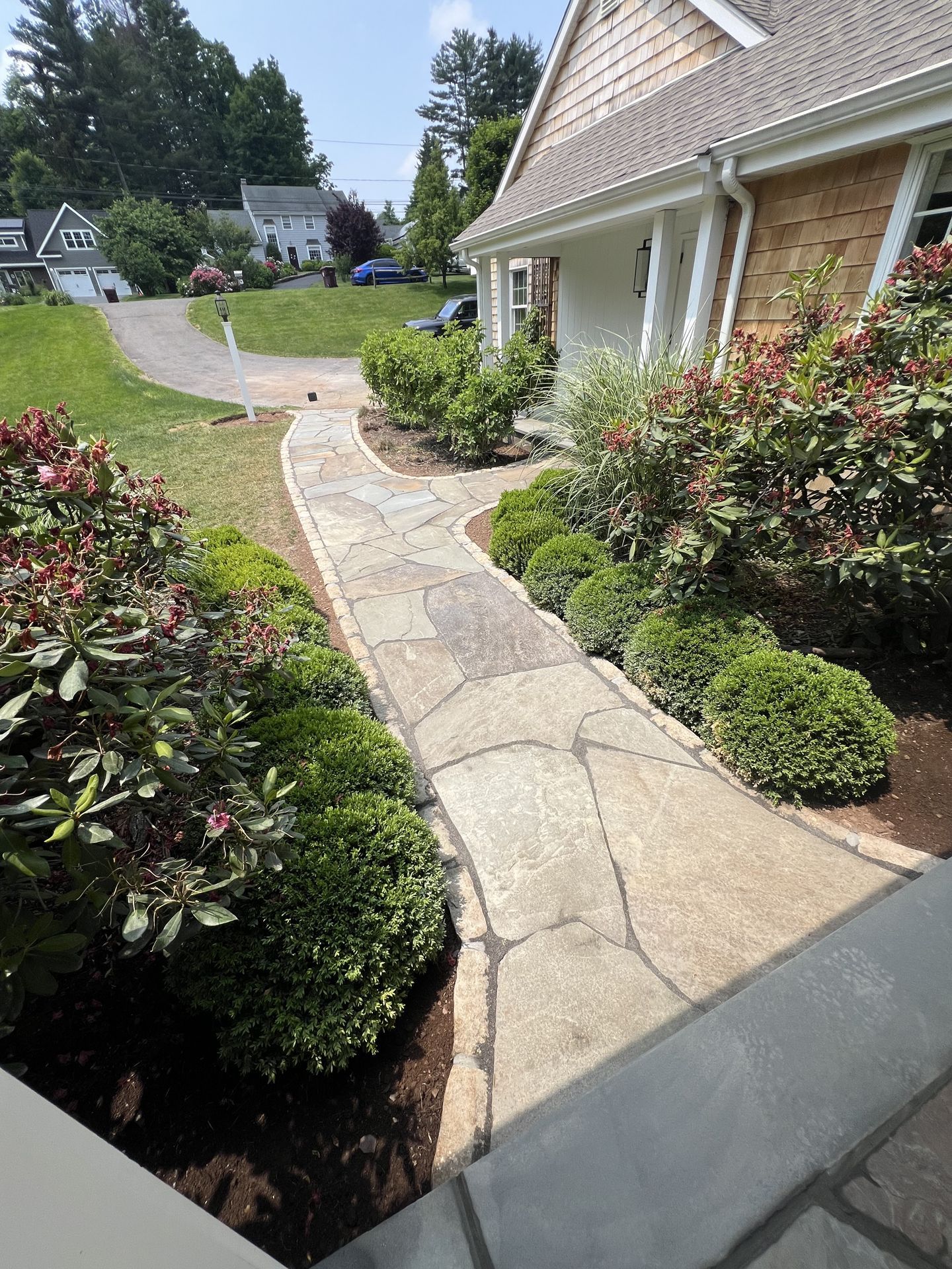 Curved stone walkway beside a house with shrubs and a landscaped front yard