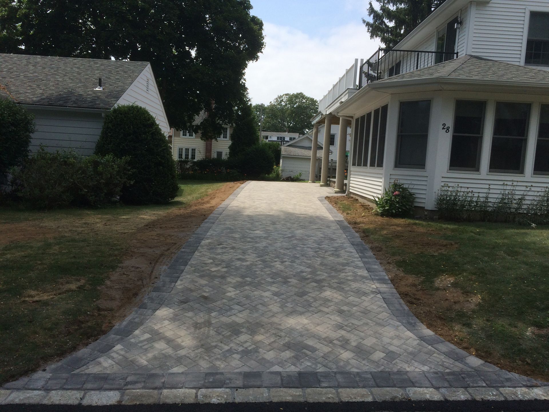 Curved brick walkway between white houses and trees on a residential street
