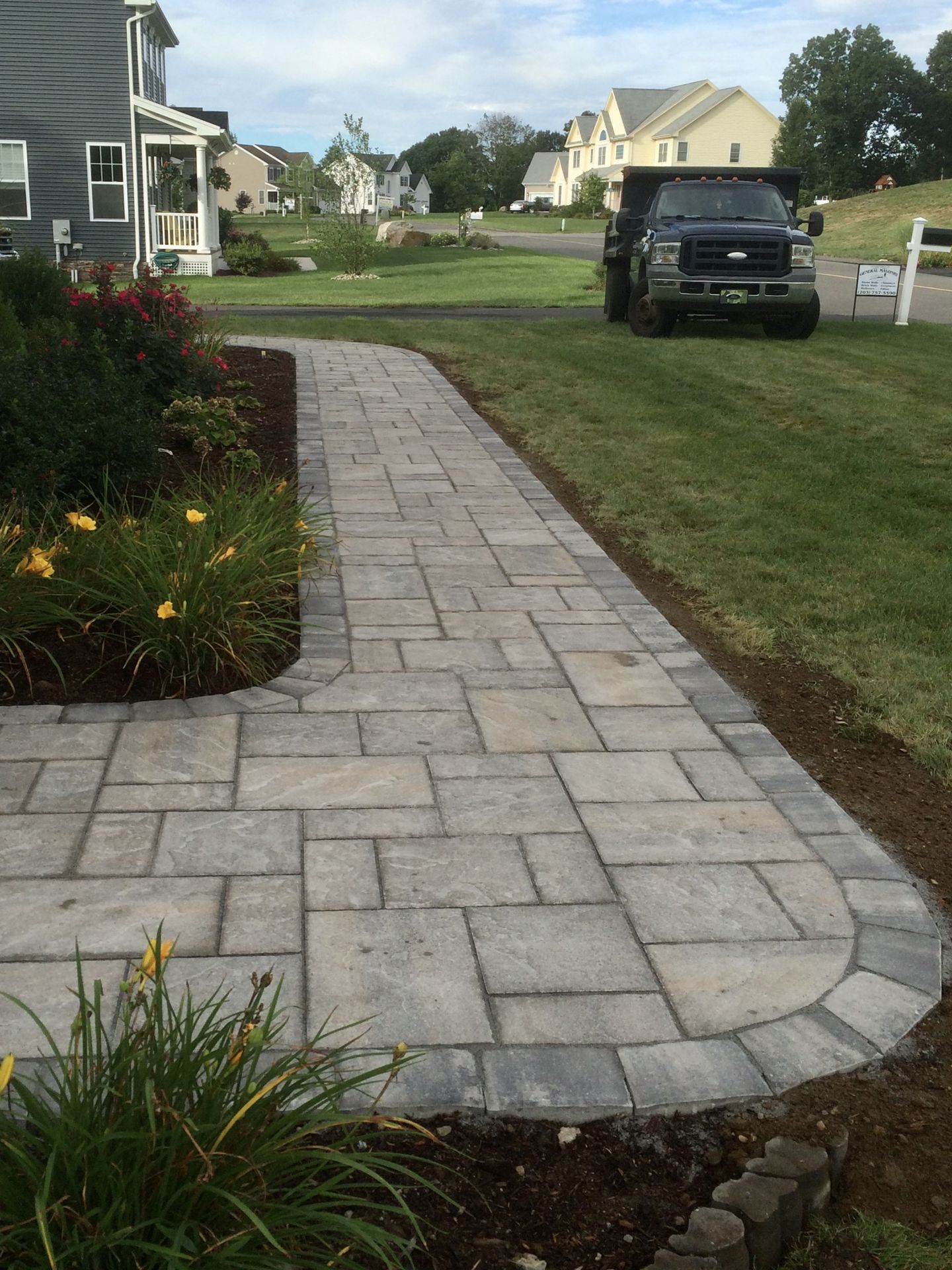 Stone walkway leading through suburban front yards with parked SUV in the background