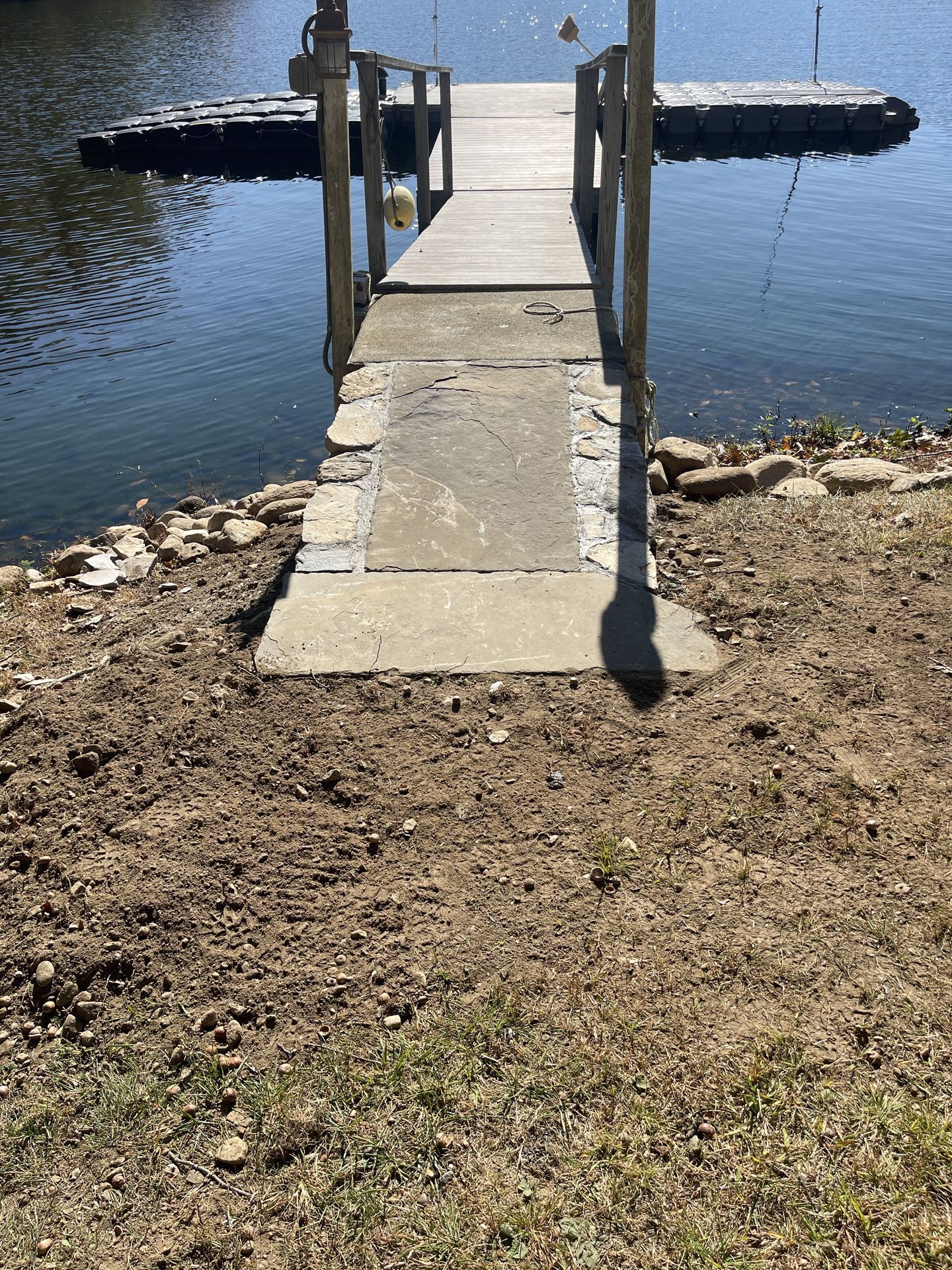 Wooden dock extending into calm blue water, with a narrow path from a rocky shore.
