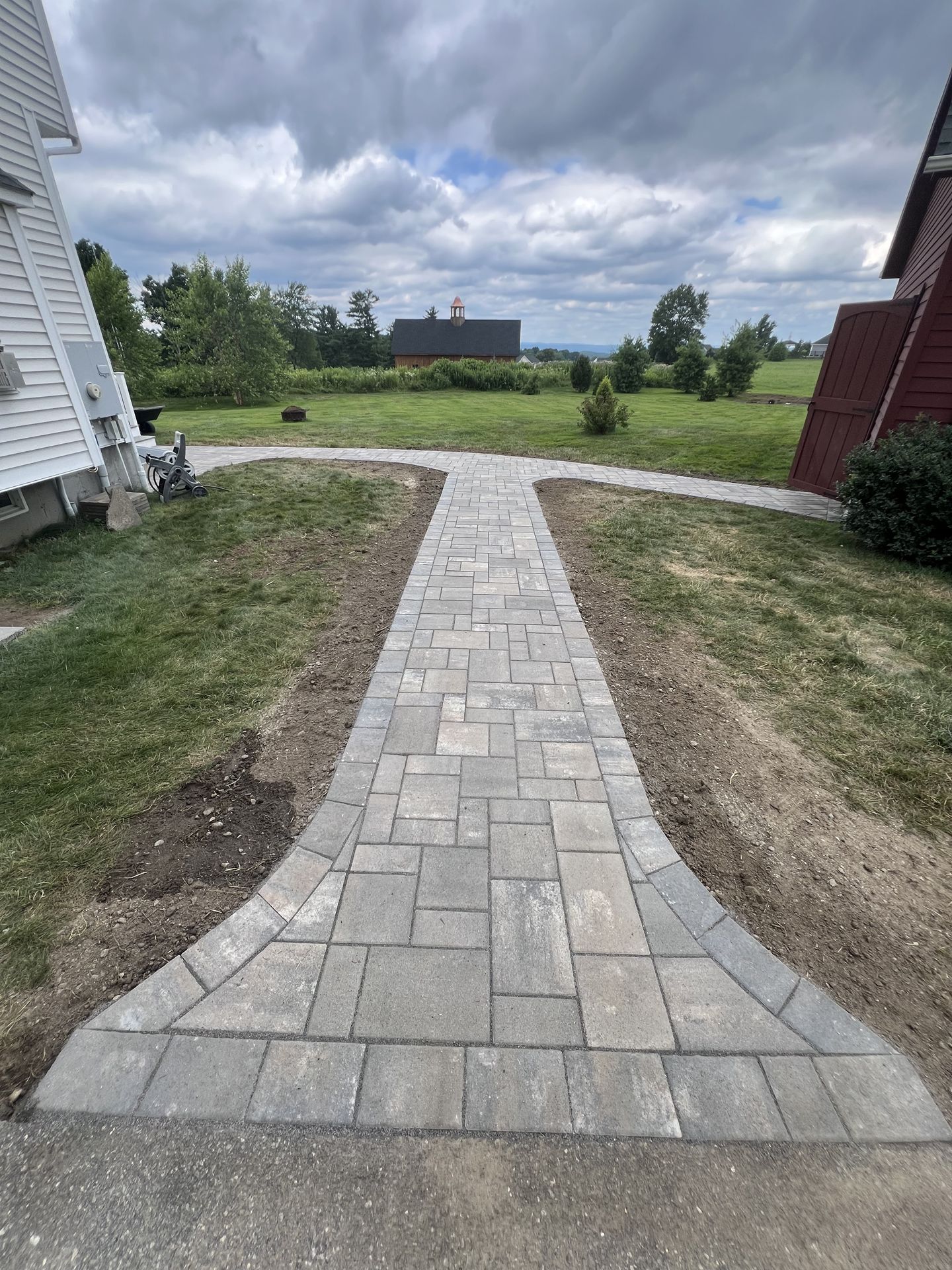 Stone walkway leading from a house to a grassy yard under a cloudy sky