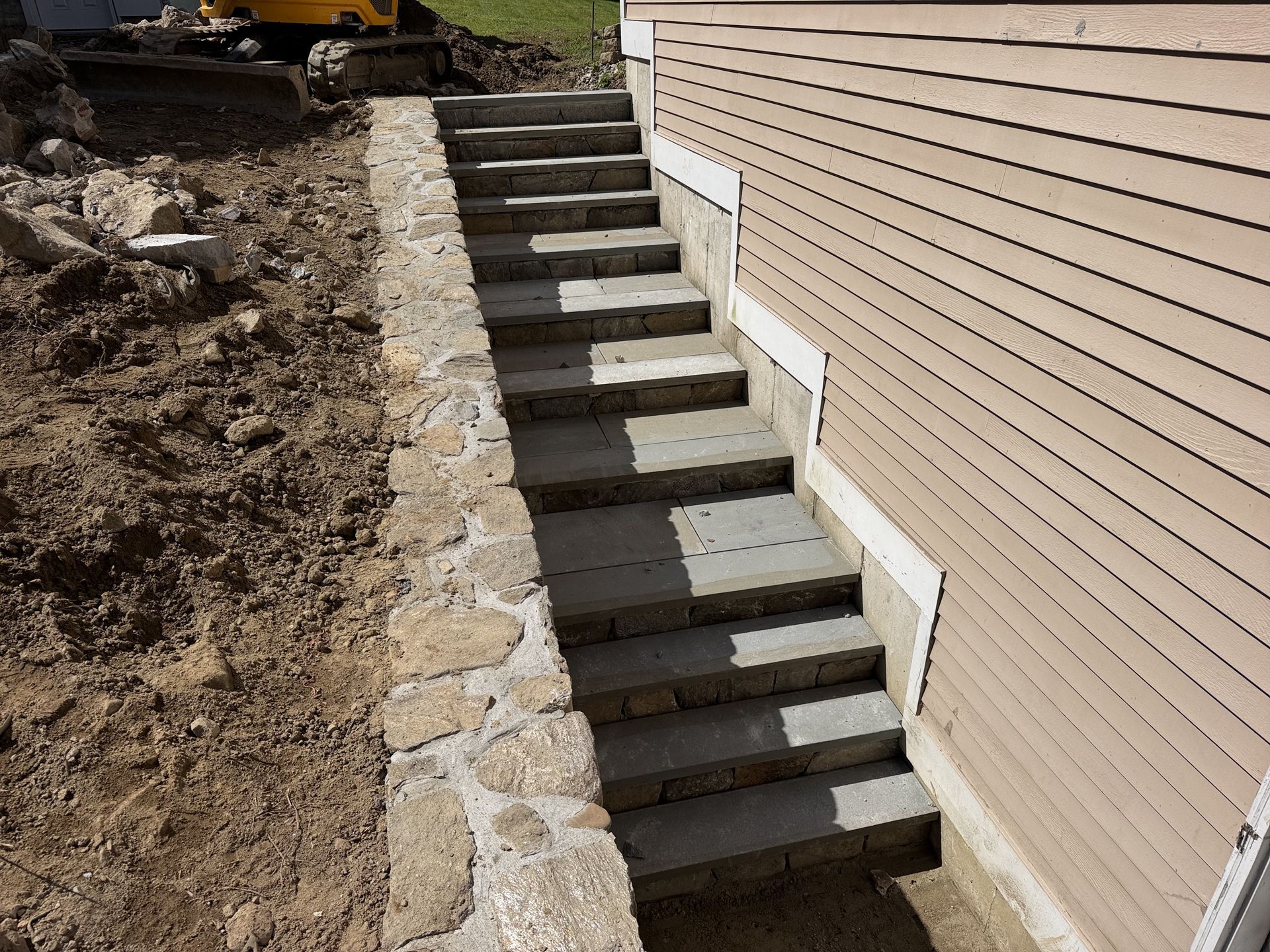 Outdoor concrete stairway with stone retaining wall beside a beige house