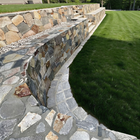 Stone retaining wall with curved stone steps beside a neatly trimmed green lawn.