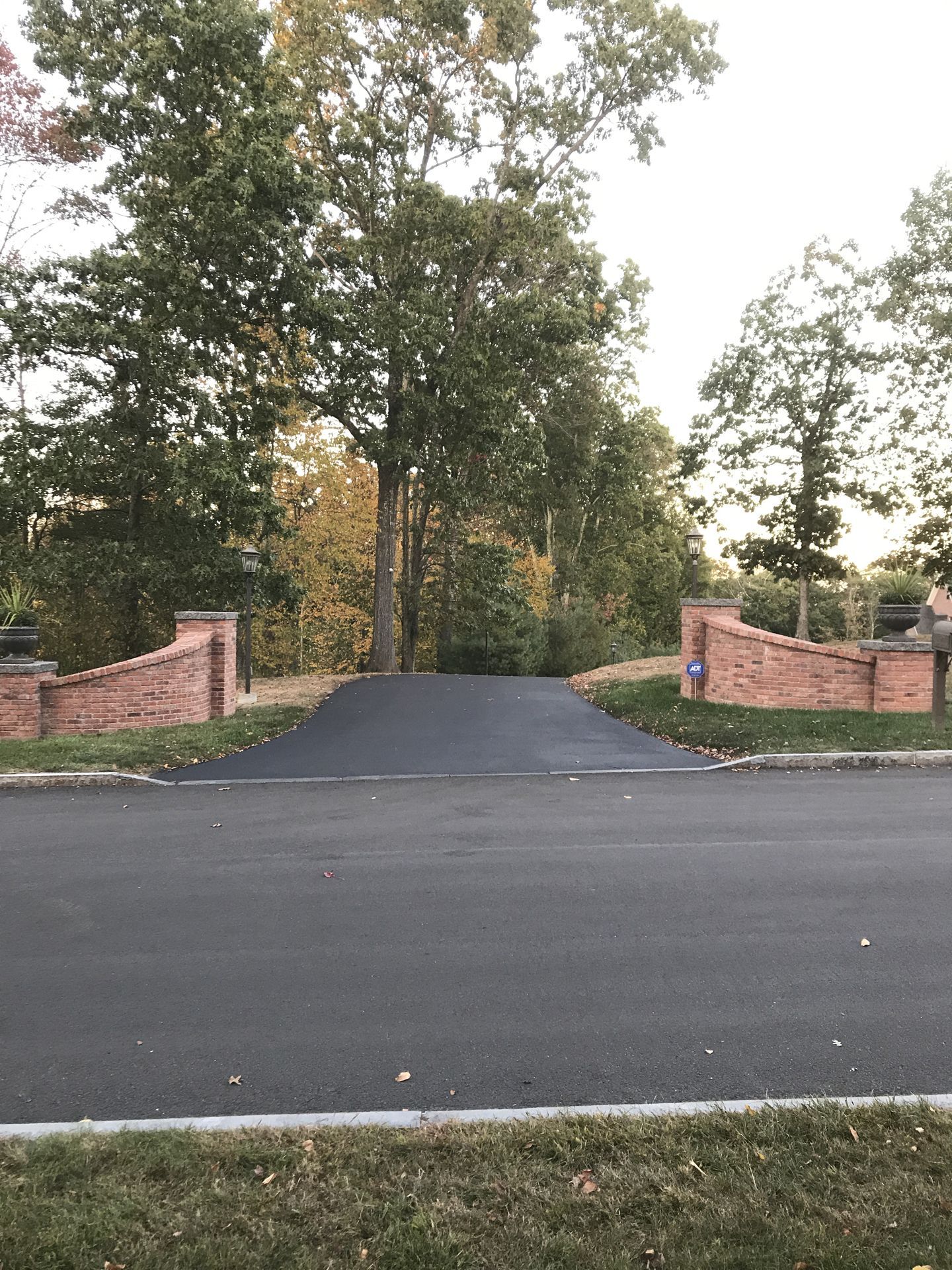 Brick-pillared driveway entrance with black pavement leading into a tree-lined property at dusk