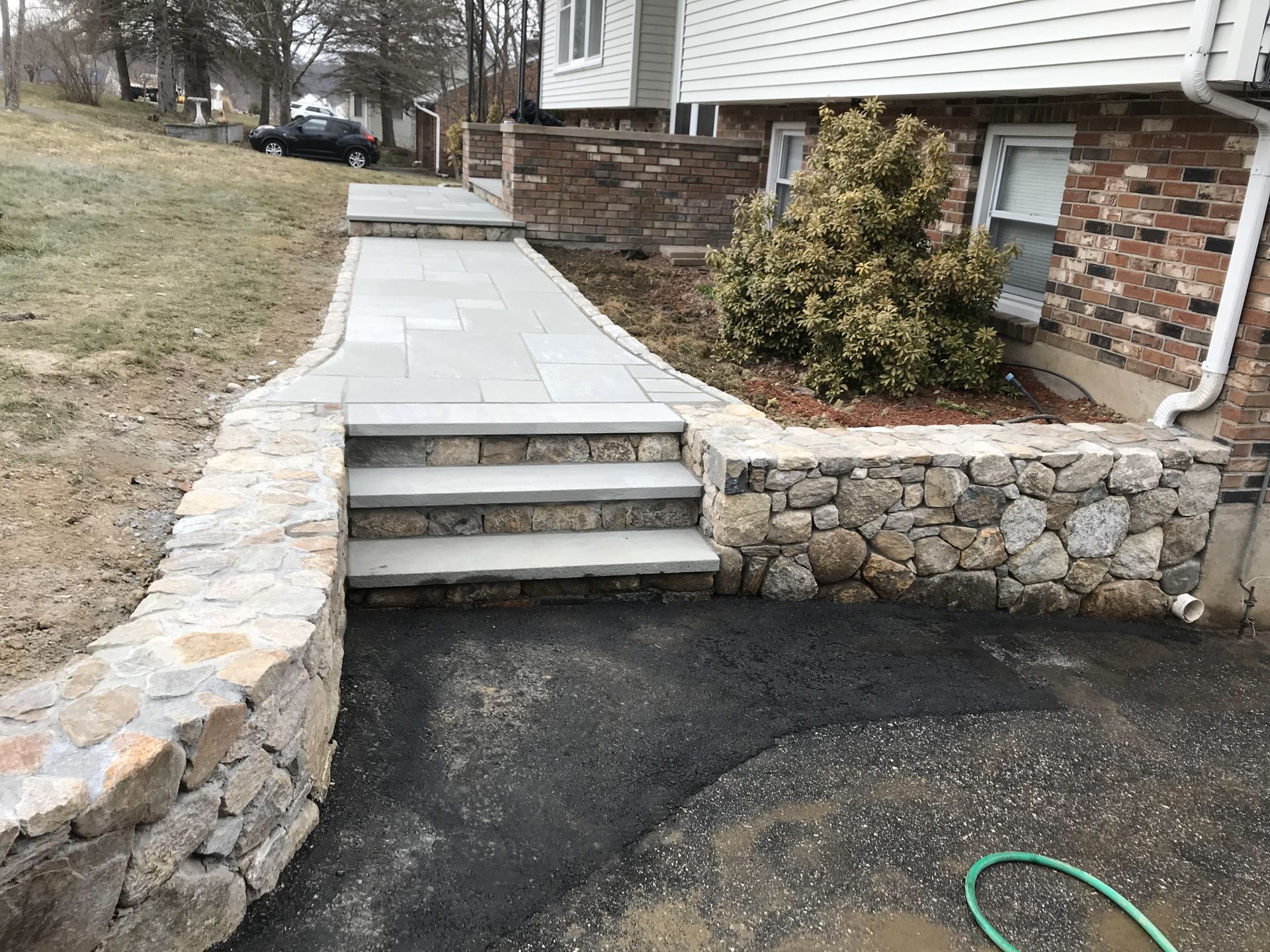 Stone walkway with steps leading to a house entrance beside a brick foundation and retaining wall