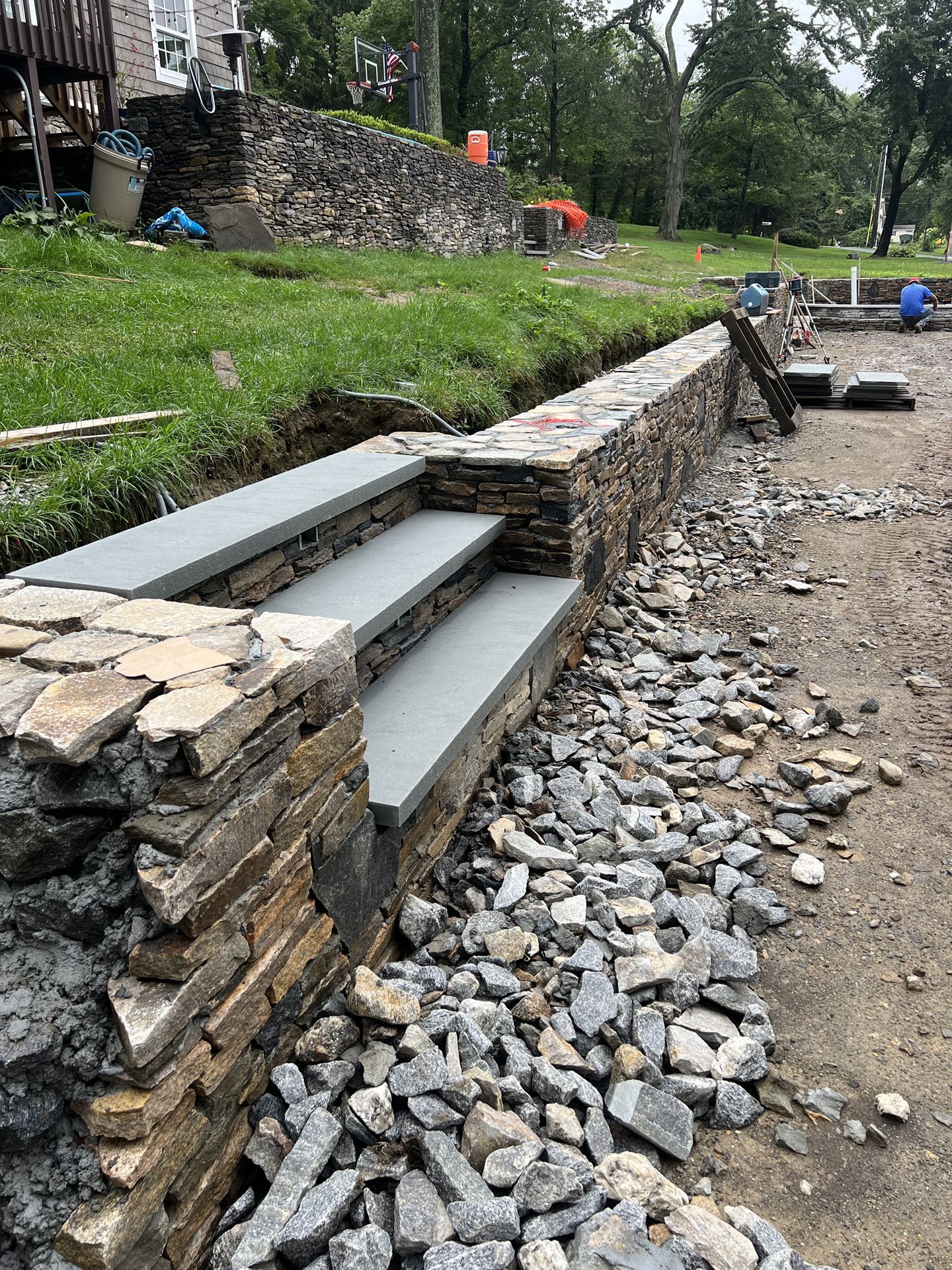Stone steps built into a retaining wall beside a rocky path and grassy area in a park-like setting
