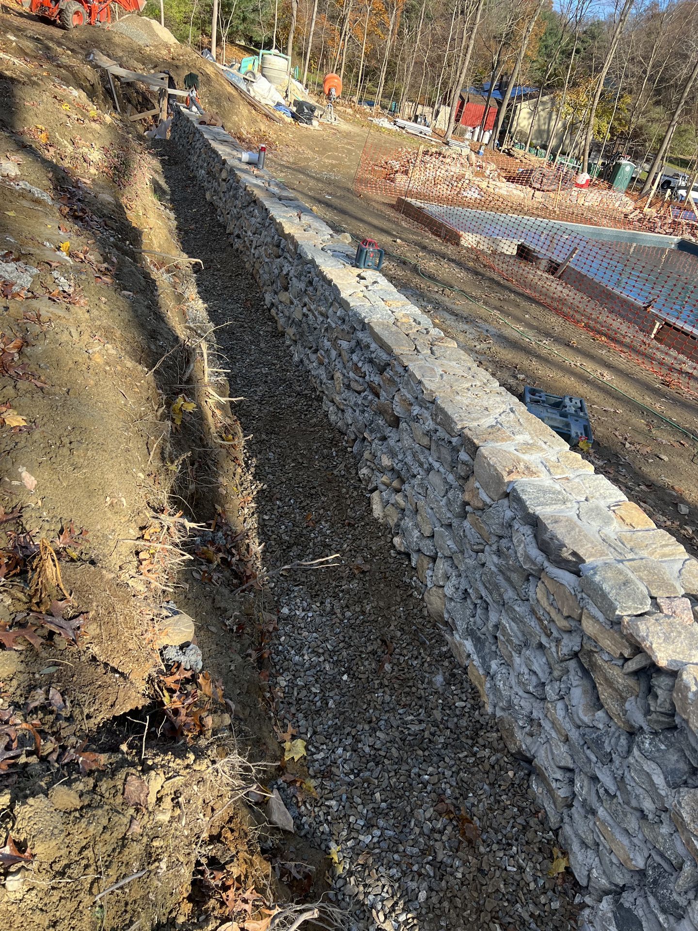 Stone retaining wall along a dirt hillside beside a muddy path in a wooded area