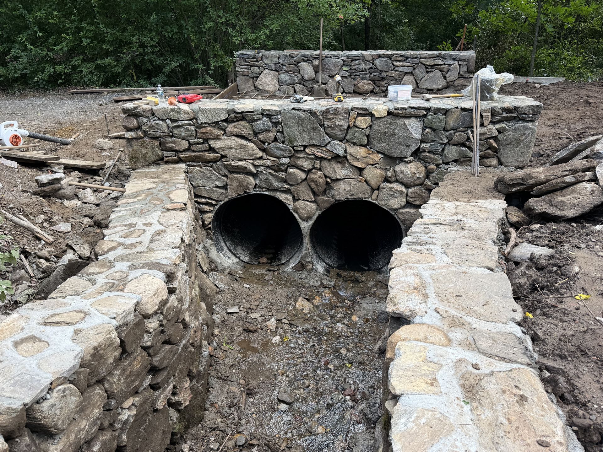 Stone culvert with two round drainage pipes in a rocky trench