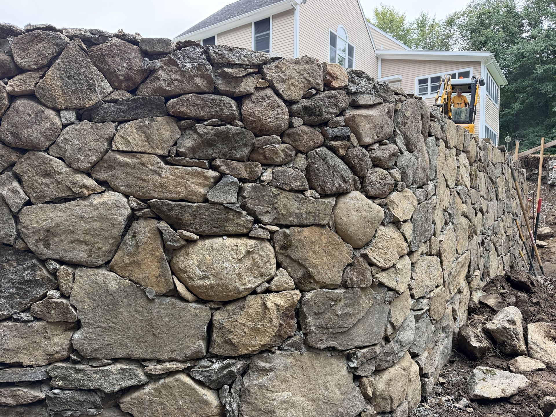 Stone retaining wall with rough boulders beside a house and walkway in a coastal neighborhood