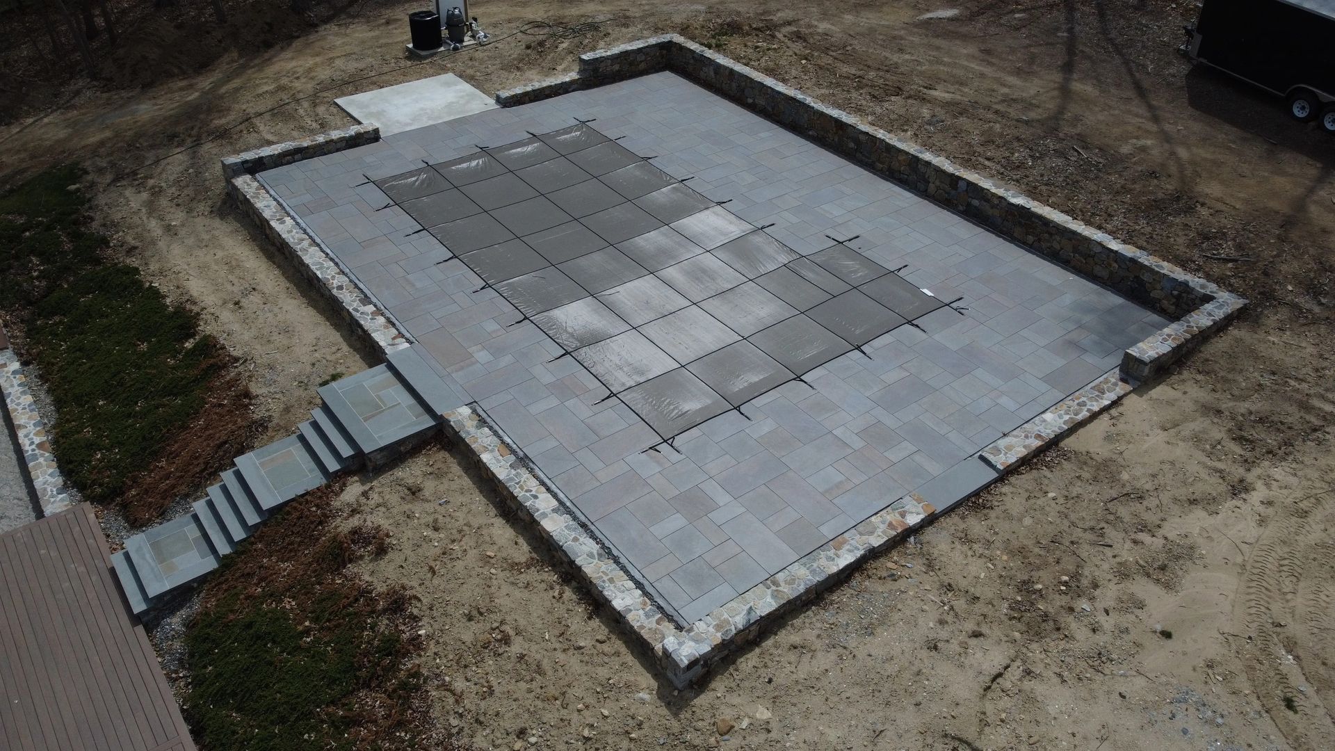 Raised concrete patio with steps and a central tiled section in a dirt yard