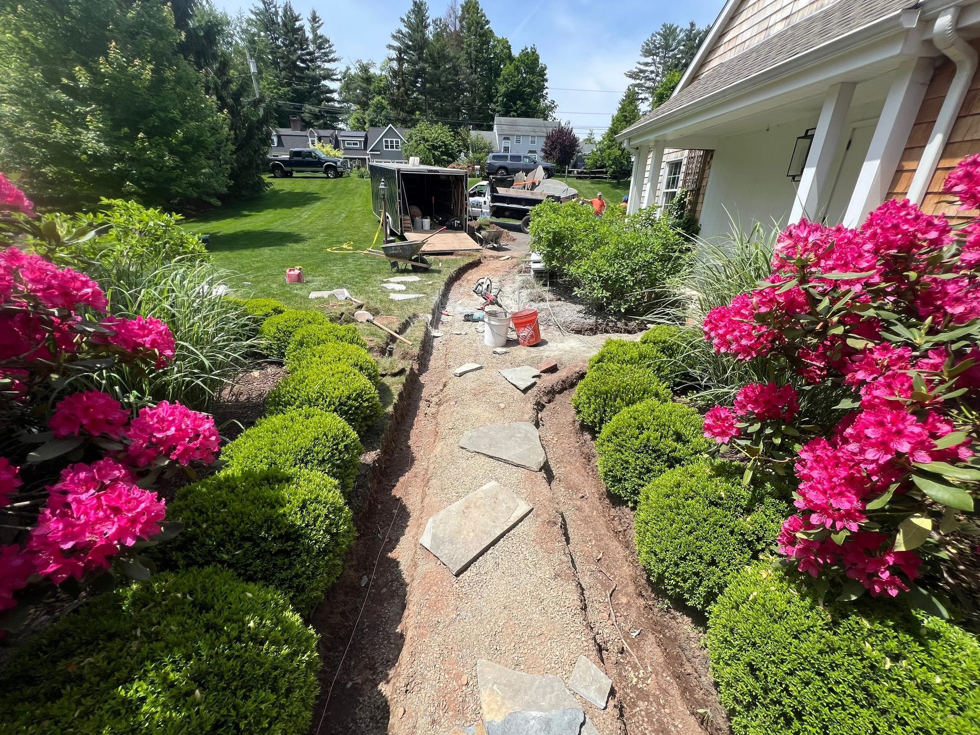 Landscaped garden path under construction beside bright pink flowering bushes and a house