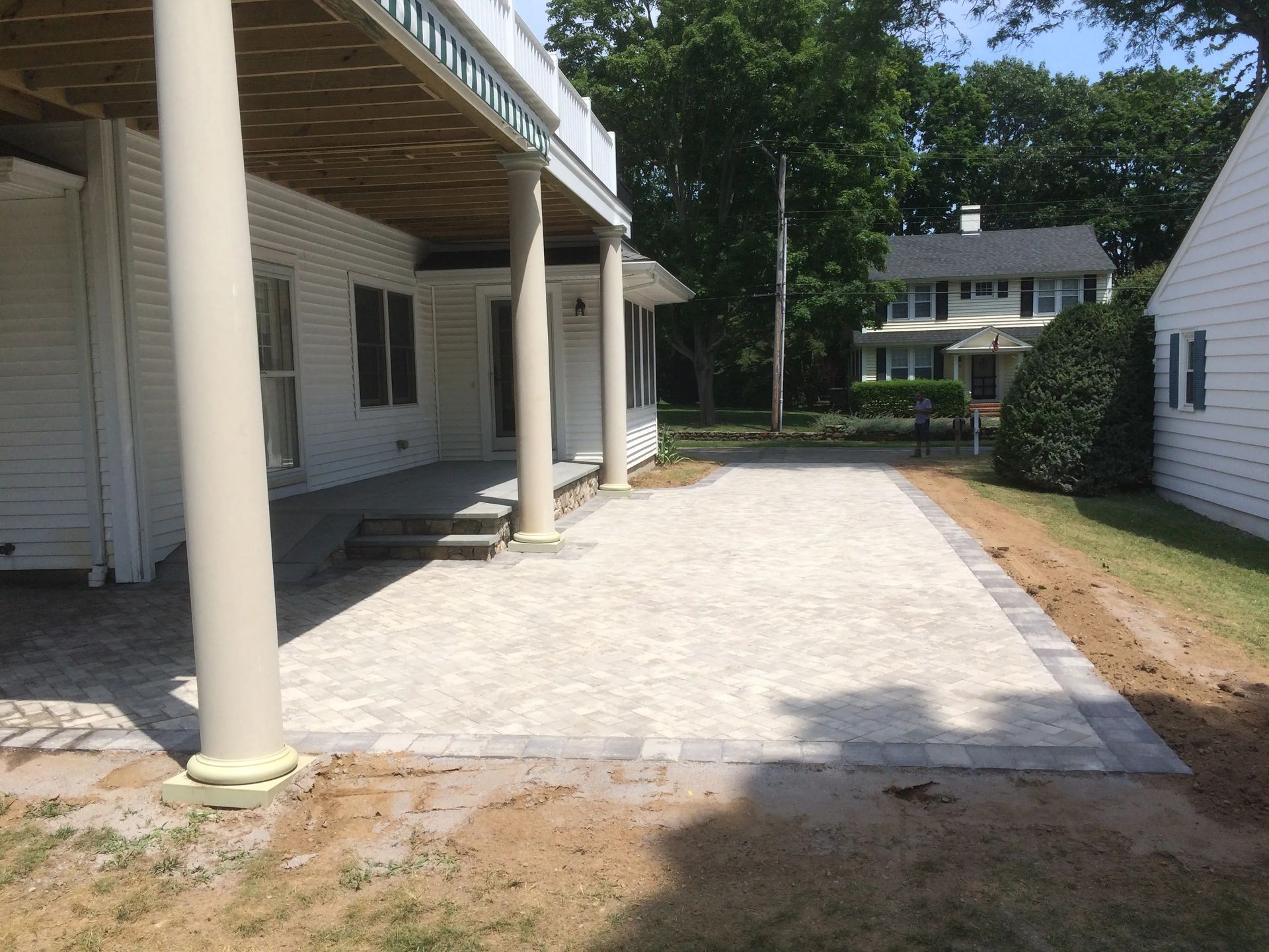 Paved driveway beside a white house with columns, leading to a backyard and another home.