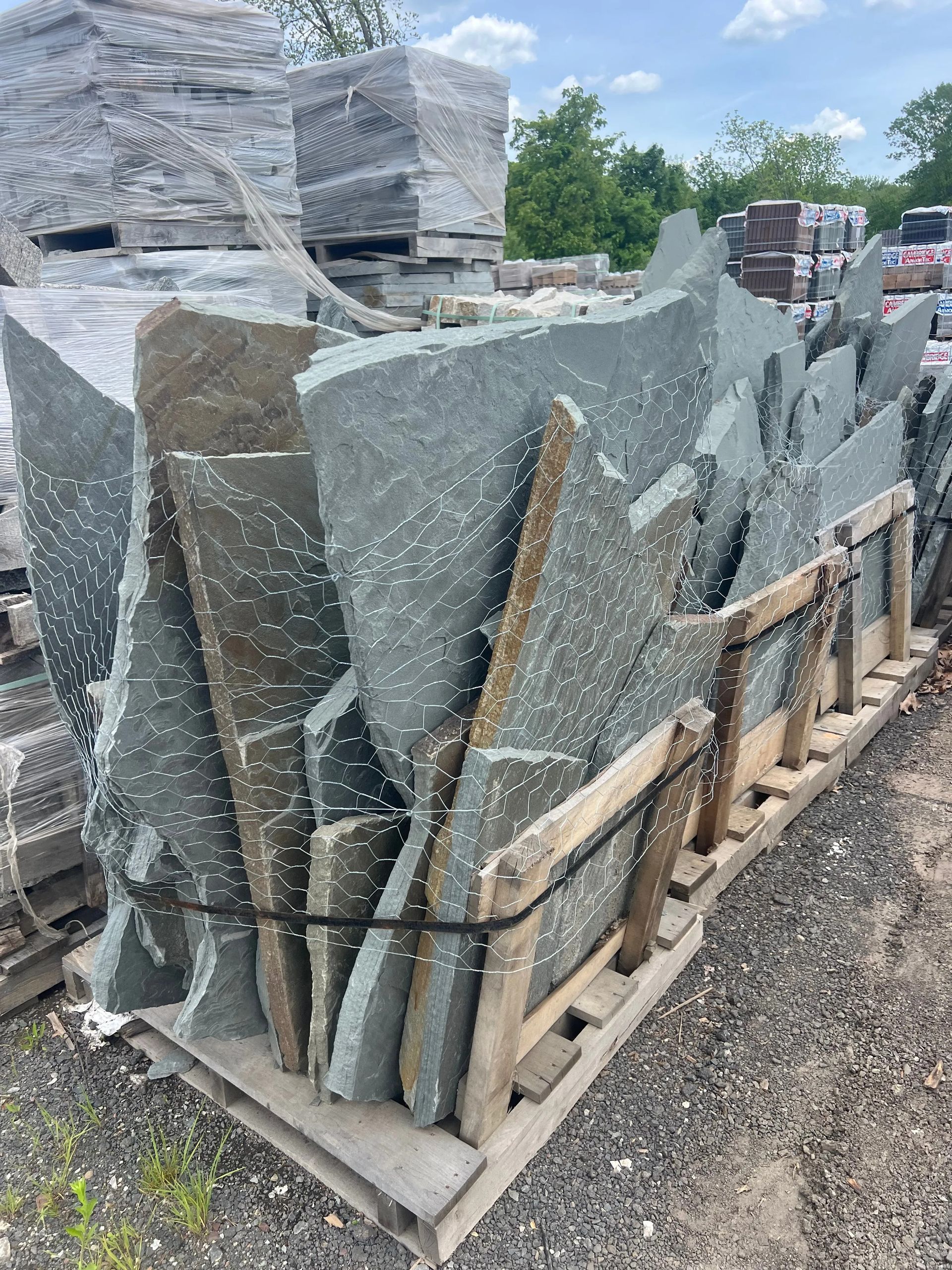 Stacked gray stone slabs strapped on a wooden pallet outdoors at a stone yard.