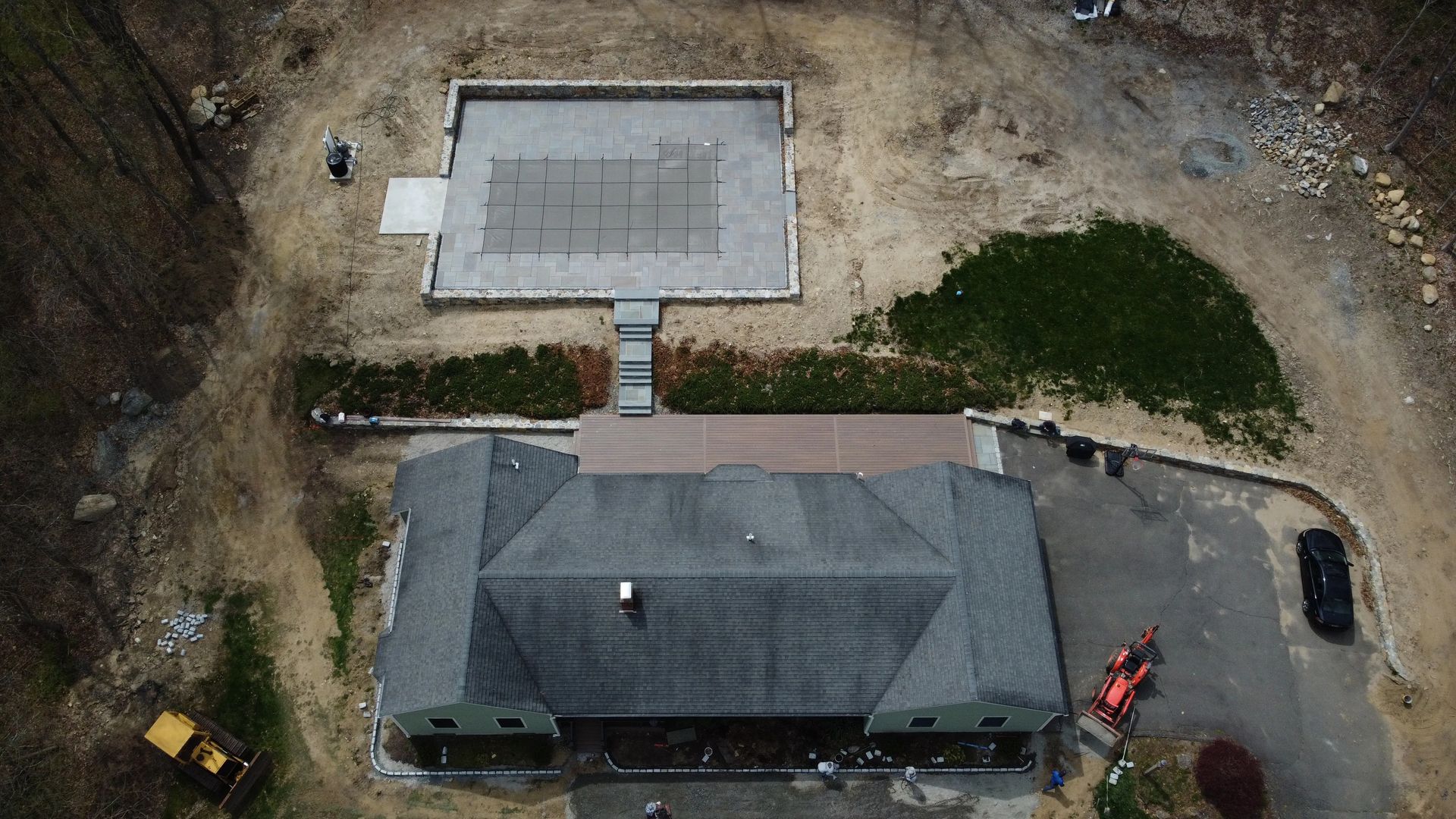 Aerial view of a house with a driveway, detached garage, and two parked vehicles on a dirt lot.