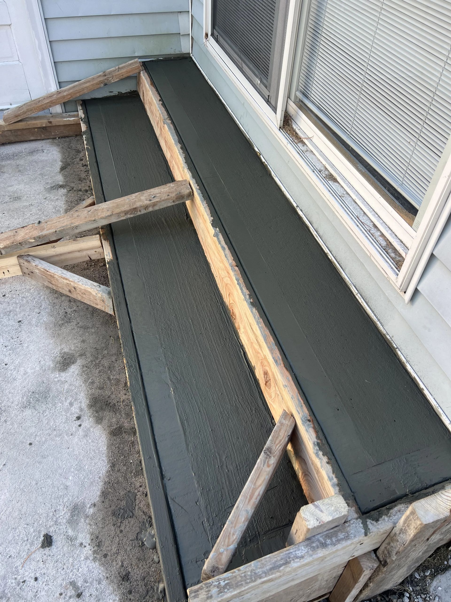 Wooden formwork holding a newly poured concrete step beside a house window