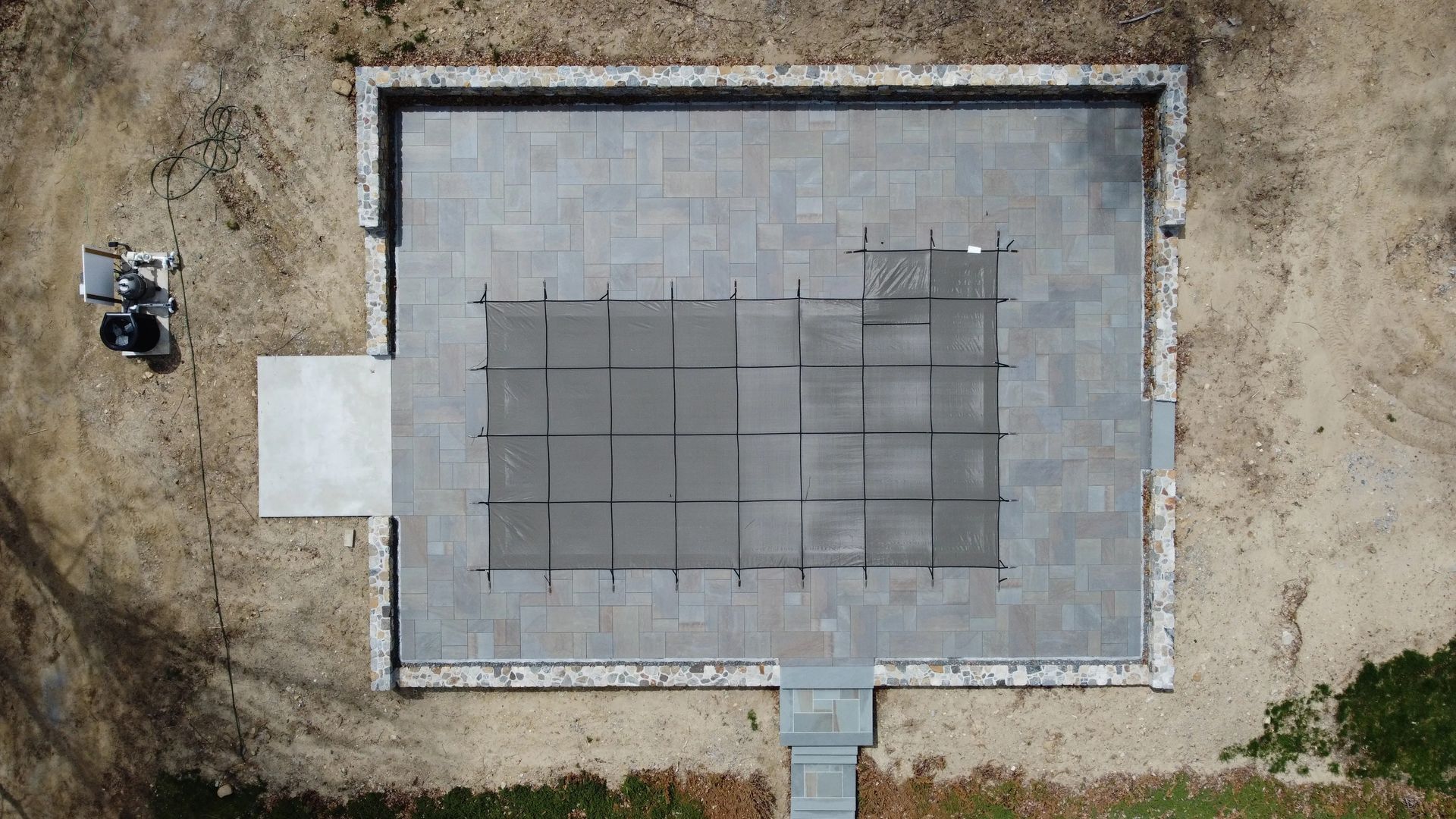 Top-down view of a concrete slab foundation with a grid pattern, surrounded by dirt and a small vehicle nearby