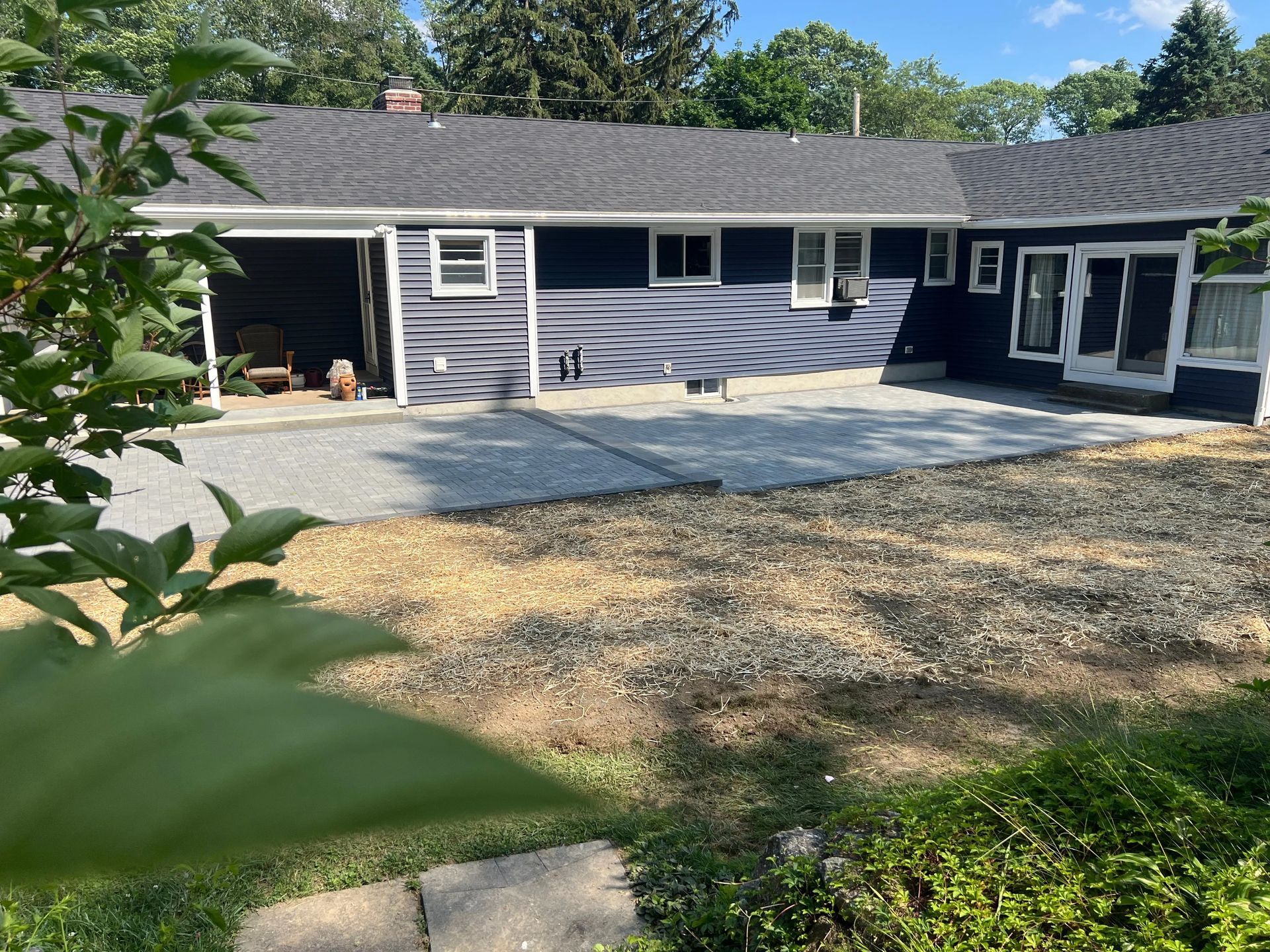 Single-story gray house with a gravel driveway, deck, and trees in the yard