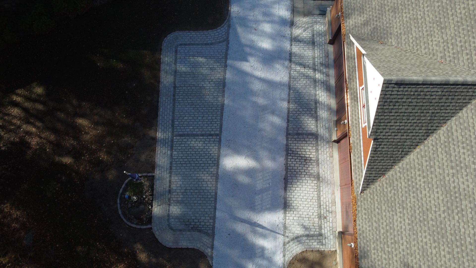 Aerial view of a rooftop with dark shingles, a metal grate, and trees beside it