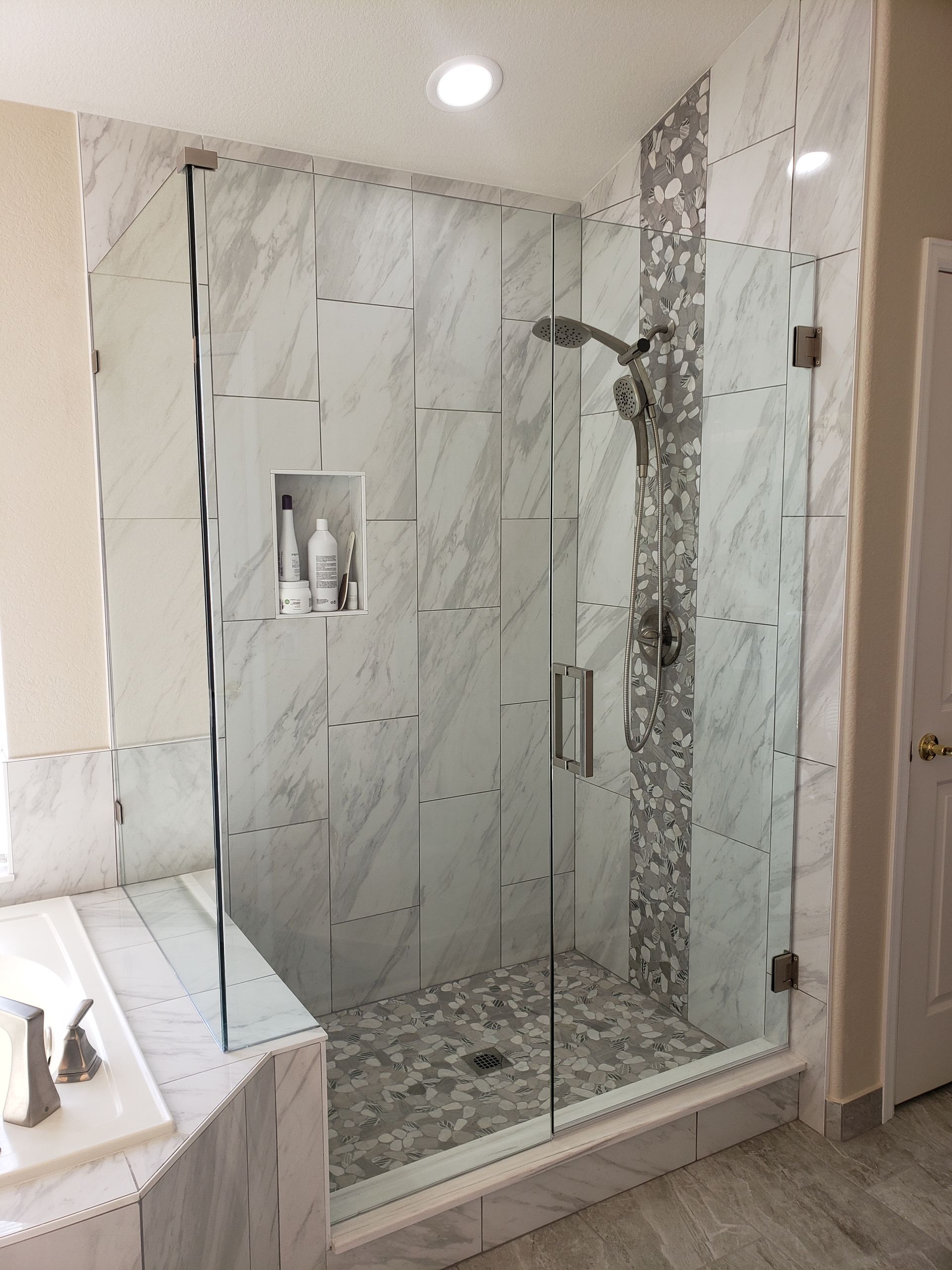 Modern bathroom shower with glass door, marble tile walls, and a built-in shelf.