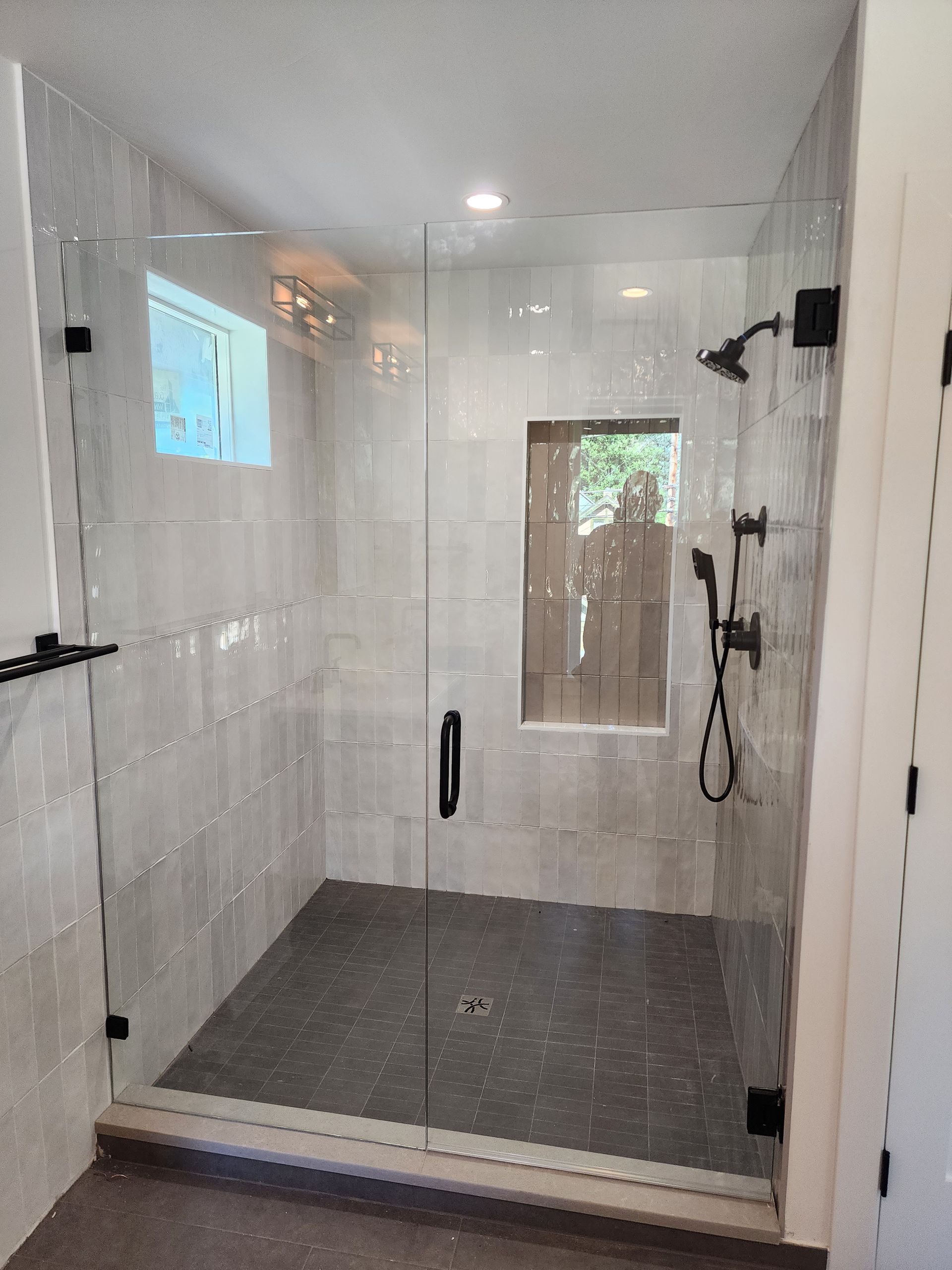 Modern walk-in shower with white tile walls, gray floor, glass door, and black fixtures.