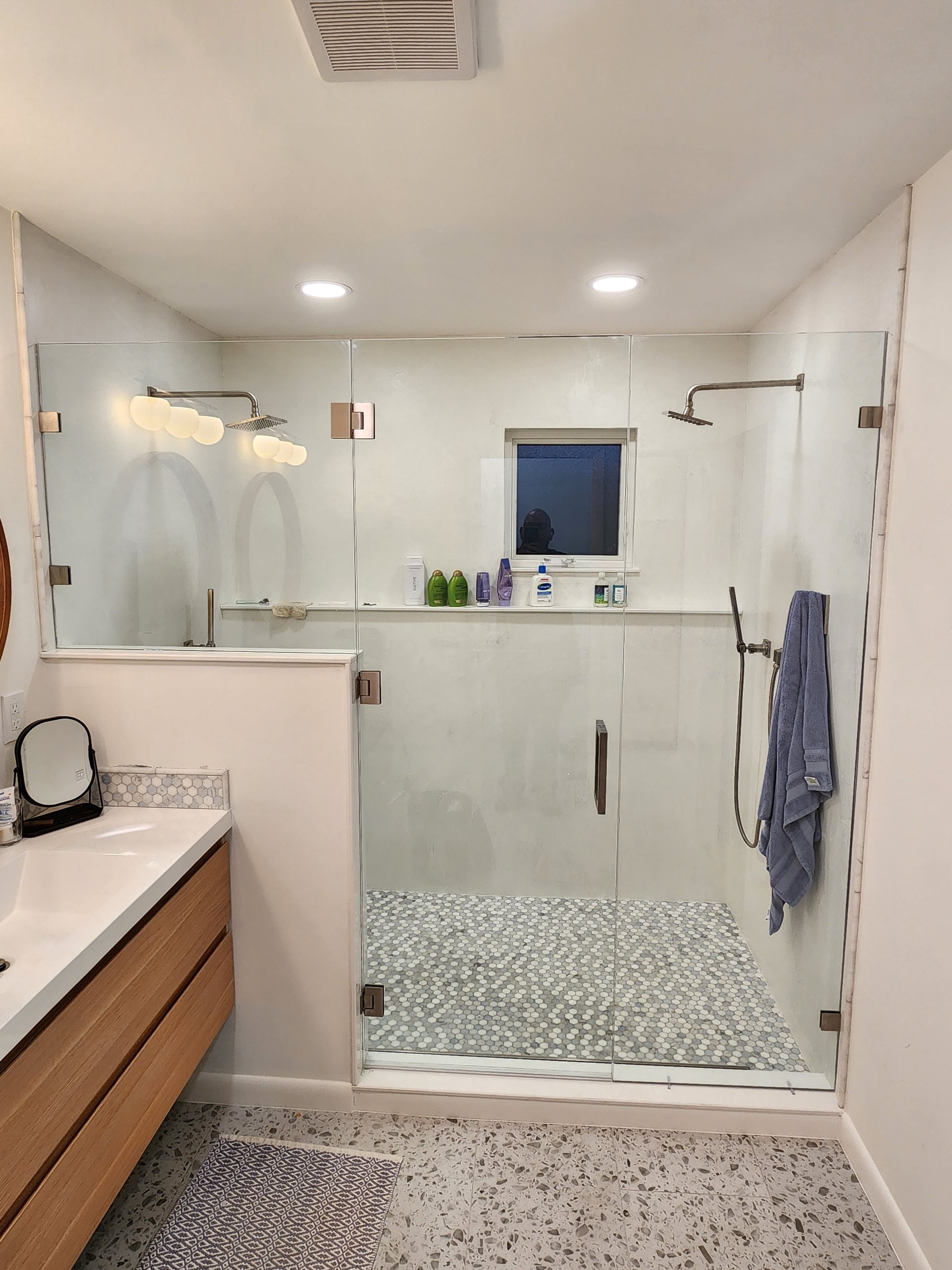 Modern bathroom with glass shower, mosaic tile floor, vanity, and towel hanging on the wall