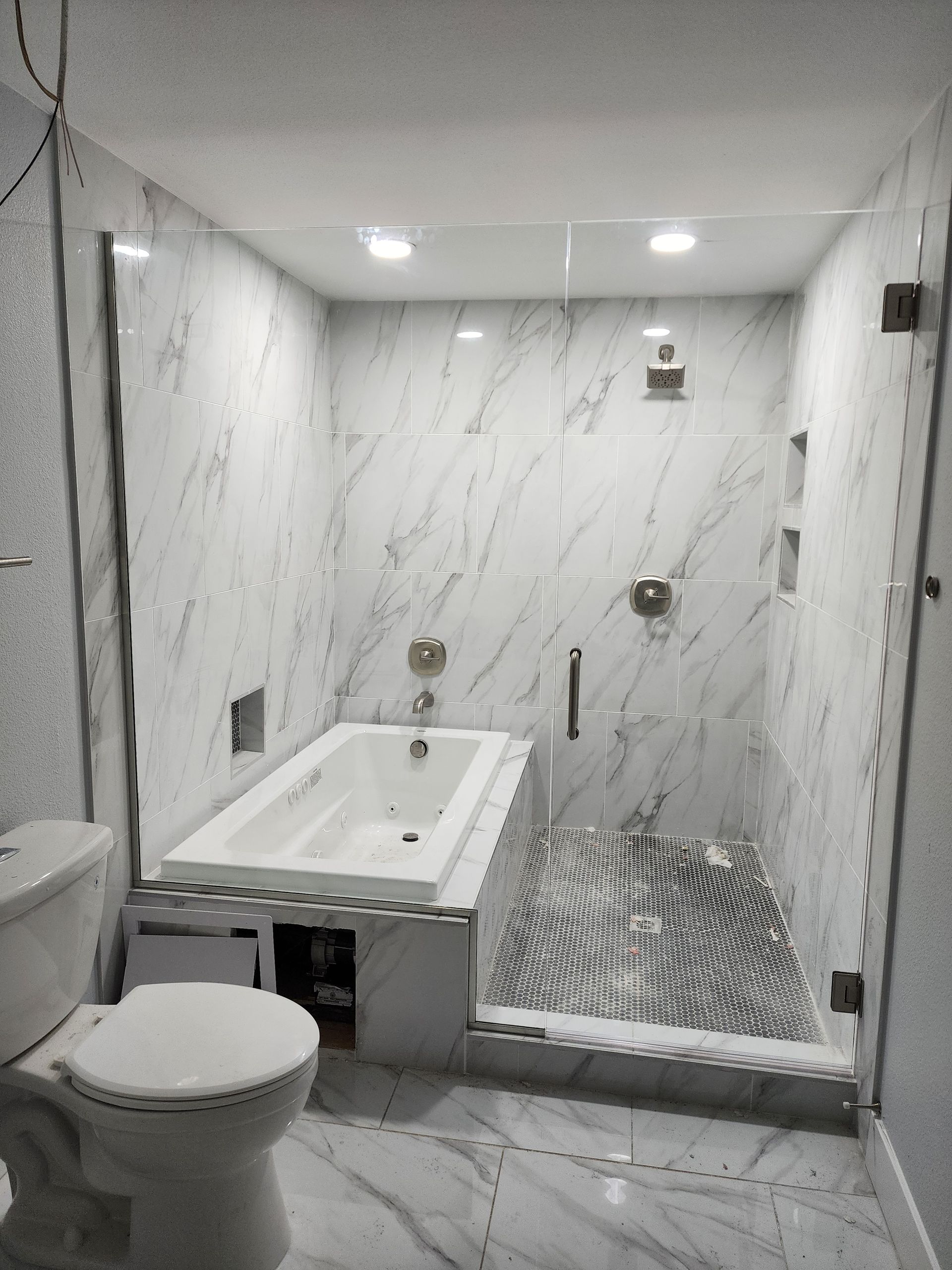 Small modern bathroom with white marble walls, toilet, sink, and a walk-in shower with striped floor tile.