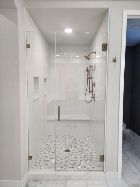 Modern white tiled shower with glass enclosure, pebble floor, and handheld showerhead