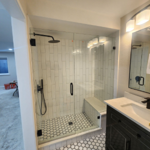 Modern bathroom with a glass walk-in shower, white tile, black fixtures, and a vanity mirror sink.