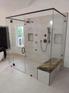 Modern walk-in shower with glass walls, black fixtures, and a built-in bench in a bright tiled bathroom