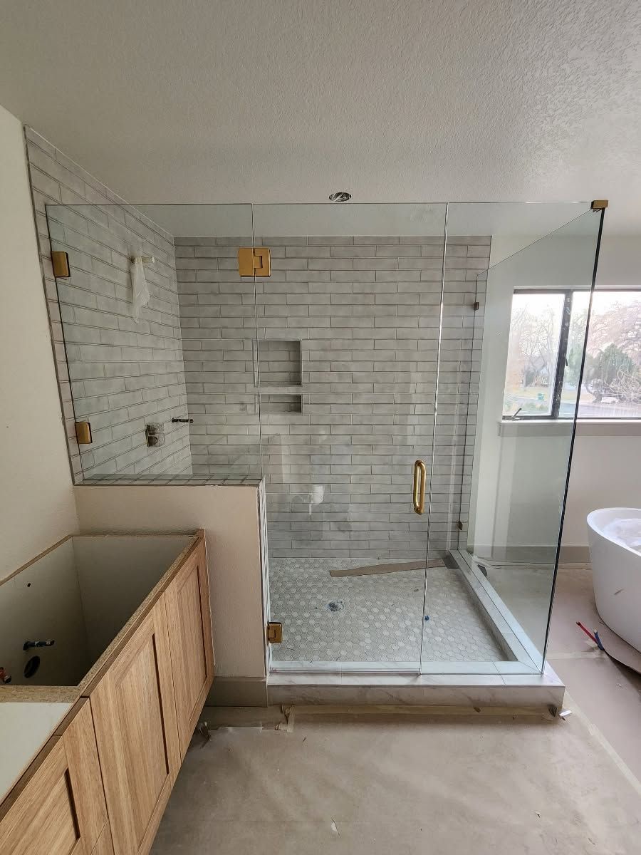 Partially renovated bathroom with glass shower, white tile, wood vanity, and tub beside a window