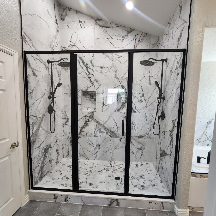 Glass shower enclosure in a modern bathroom with gray tile walls and built-in benches
