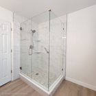 Glass corner shower enclosure in a bright bathroom with white tile and beige flooring