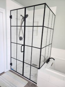 Black-framed shower enclosure with clear panels beside a bathtub in a white bathroom.