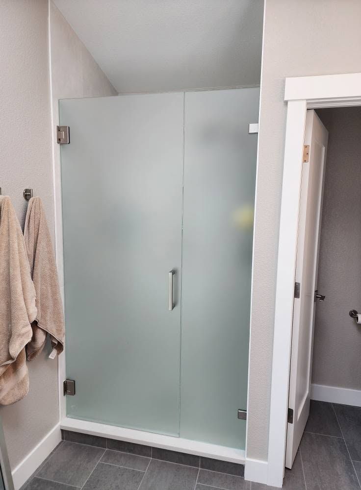 Glass shower enclosure in a modern bathroom with gray tile walls and built-in benches