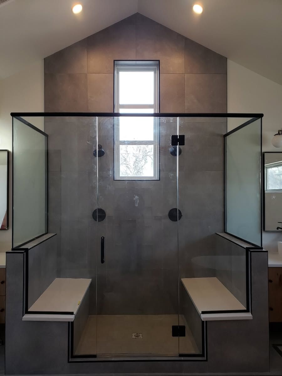 Glass shower enclosure in a modern bathroom with gray tile walls and built-in benches