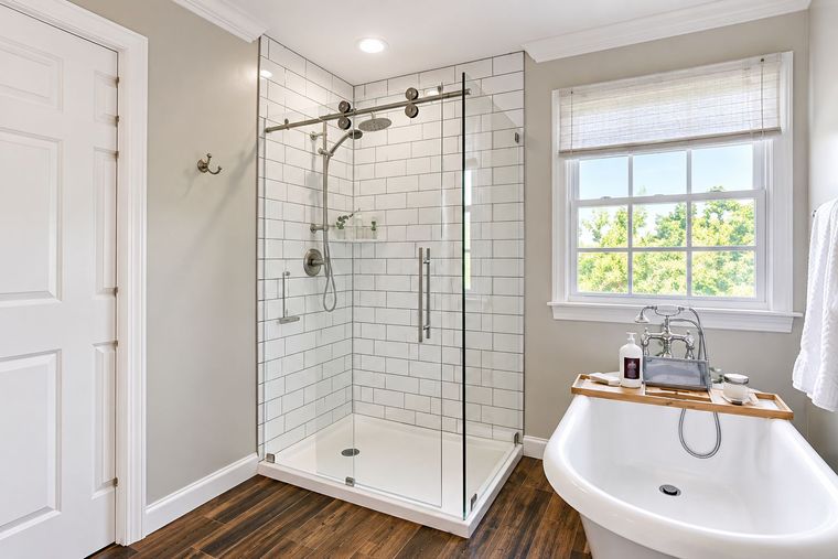 Modern bathroom with glass shower enclosure, tiled walls, and bathtub by a window.