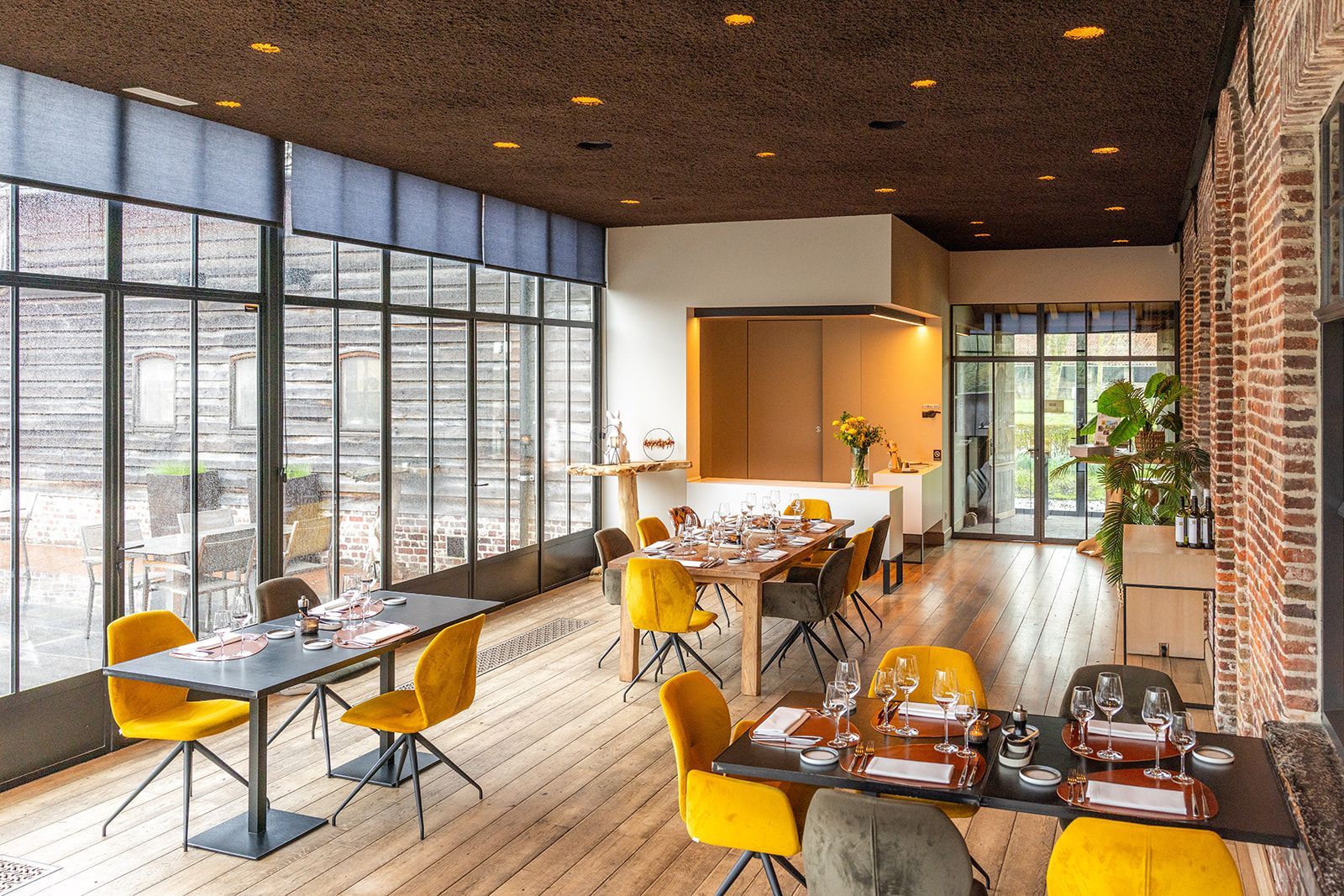 A restaurant interior with wooden floors, mustard yellow chairs, and large window panels looking out to a patio.